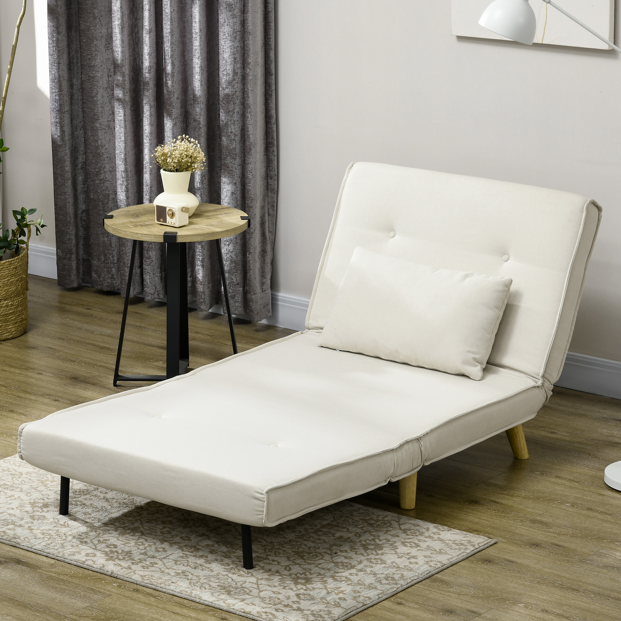 Una chaise longue color crema con una almohada, una mesa auxiliar con flores y cortinas grises al fondo.