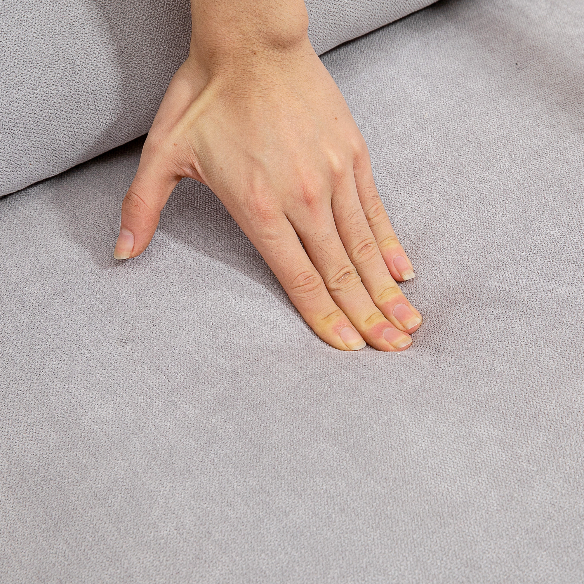 Una mano descansa sobre una tela gris. La mano es de piel clara con uñas visibles. La tela parece suave y texturizada.