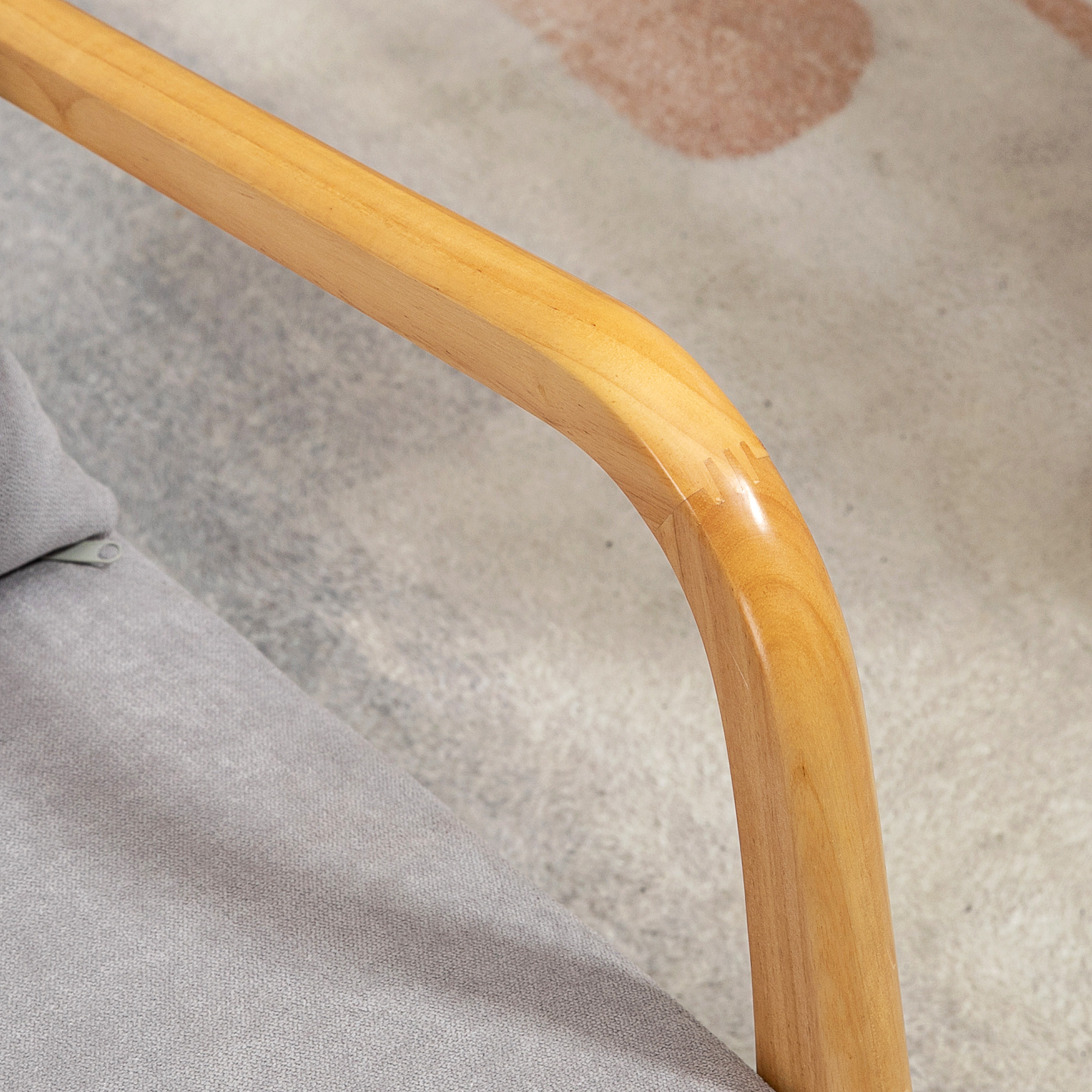 Primer plano de un reposabrazos de madera. La madera marrón claro se curva a la izquierda. Se ve un cojín gris.