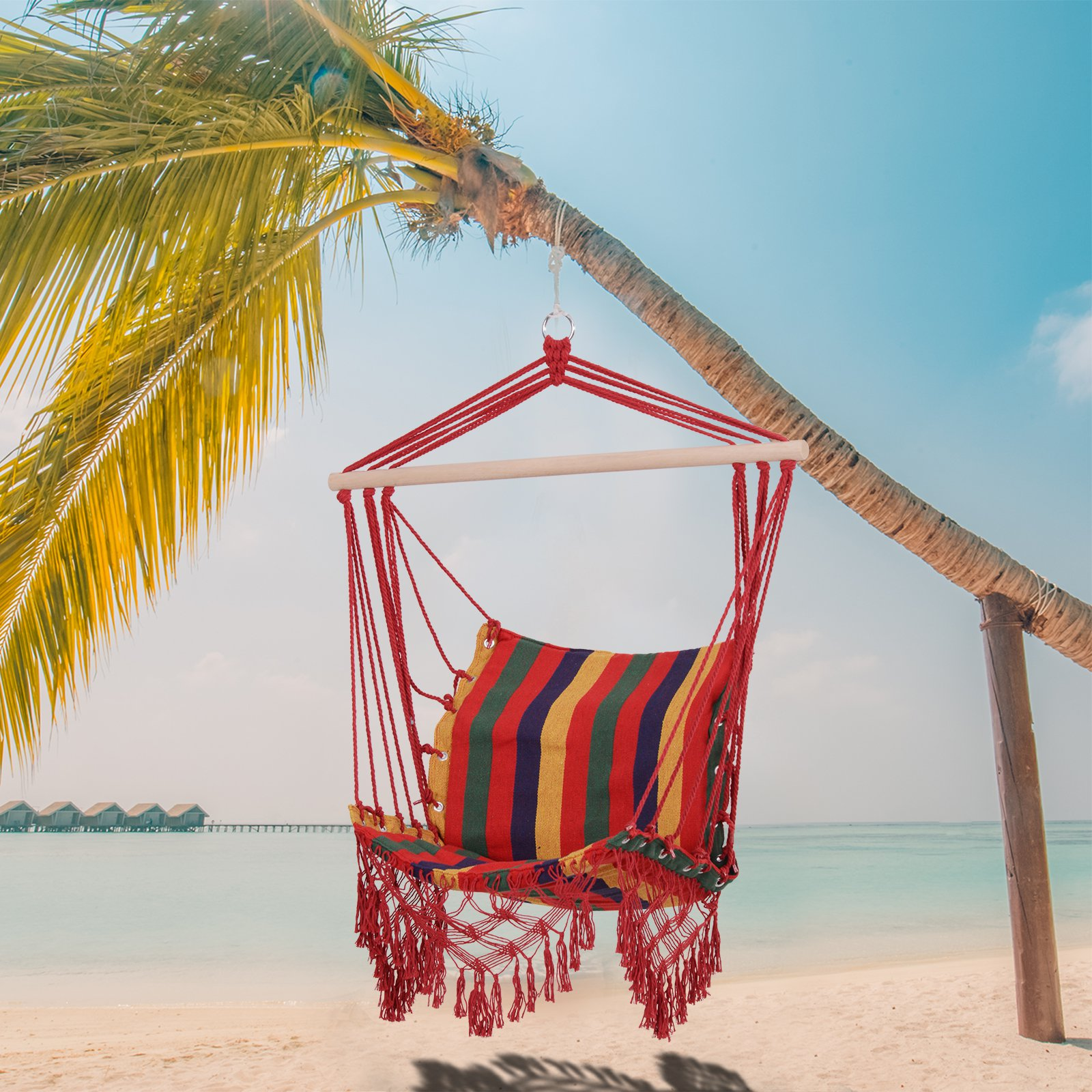 Una hamaca roja cuelga de una palmera en la playa. La hamaca tiene un cojín a rayas. El océano y el cielo están al fondo.