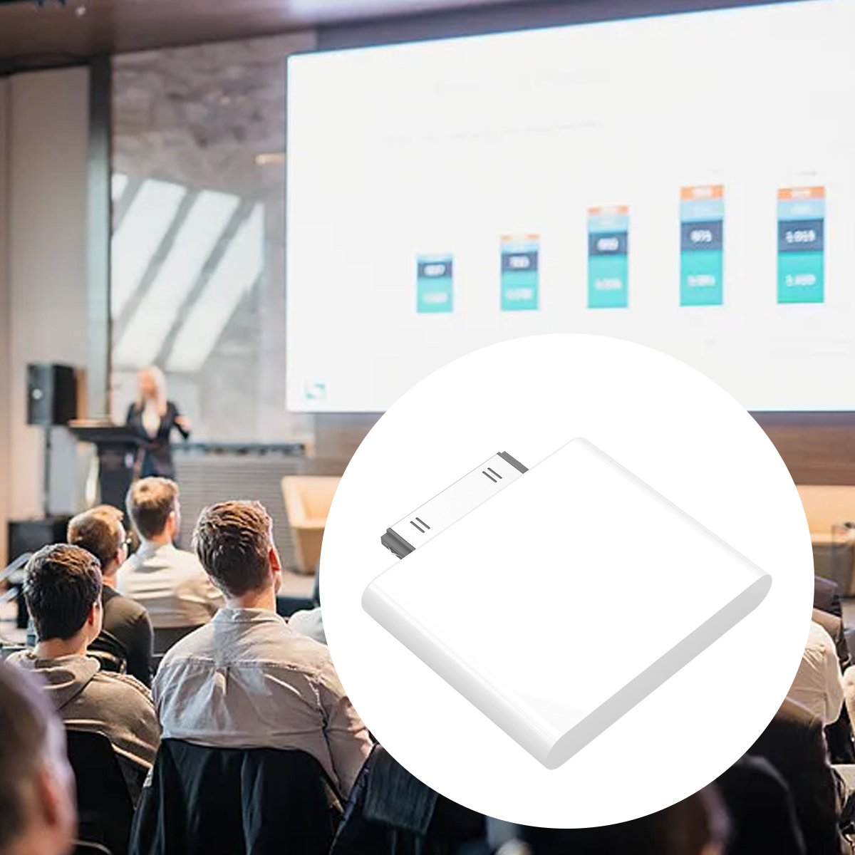 Ein weißes Gerät vor einem Konferenzraum. Menschen sitzen und sehen eine Präsentation auf einem Bildschirm.