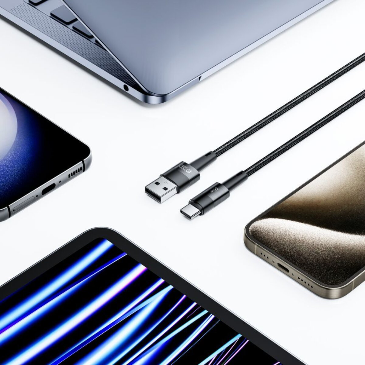 Un câble de chargement USB-C et des appareils : un ordinateur portable, un téléphone, une tablette et un autre téléphone sont disposés sur une surface blanche.