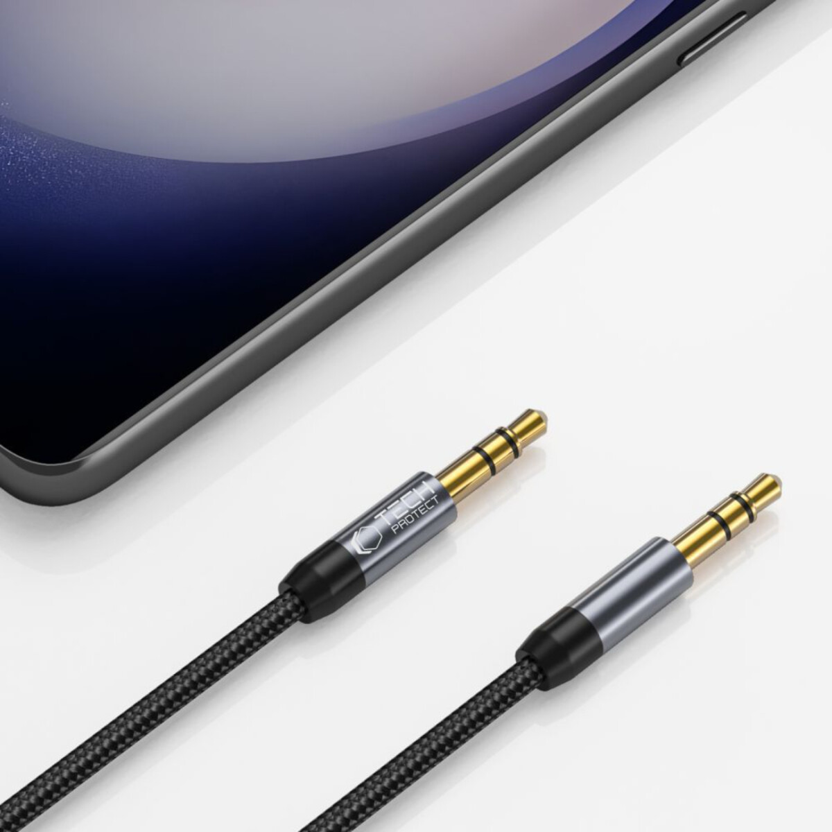 Two audio jack cables with gold connectors. A phone is in the background. Cables are black and grey.