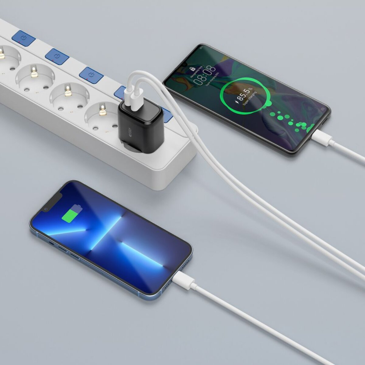 Deux smartphones en charge via une multiprise. L'un affiche 85,5% de charge, l'autre une icône de batterie en charge. Un chargeur est branché.