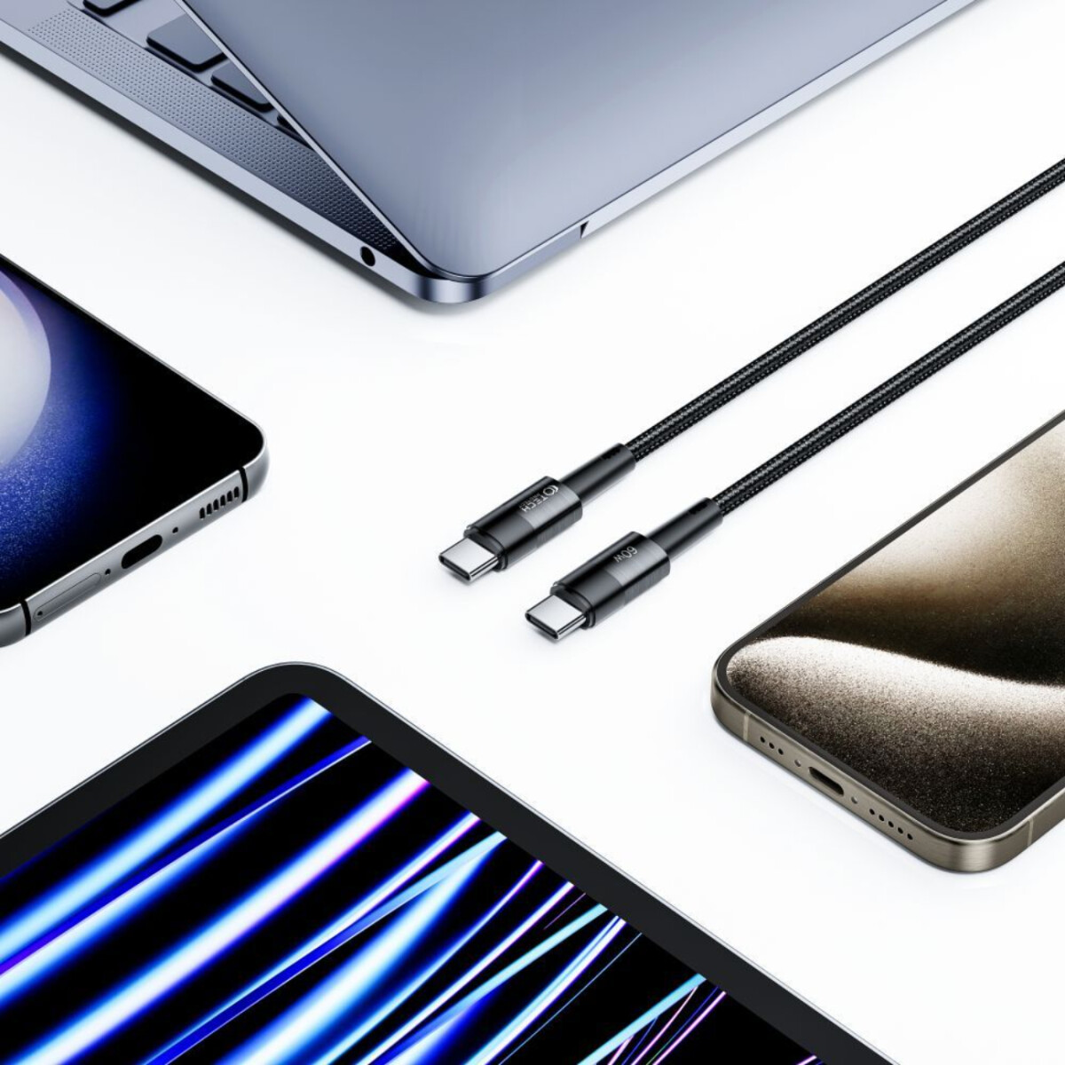 Câbles de chargement noirs avec connecteurs USB-C près d'un ordinateur portable, téléphones et tablette sur surface blanche.