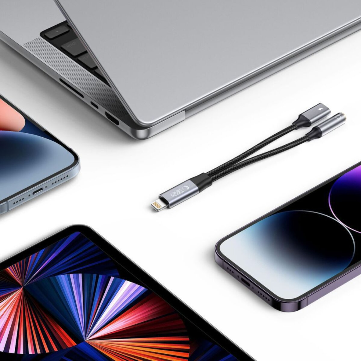 A white surface with a laptop, three smartphones, and a black and silver cable with two lightning connectors.