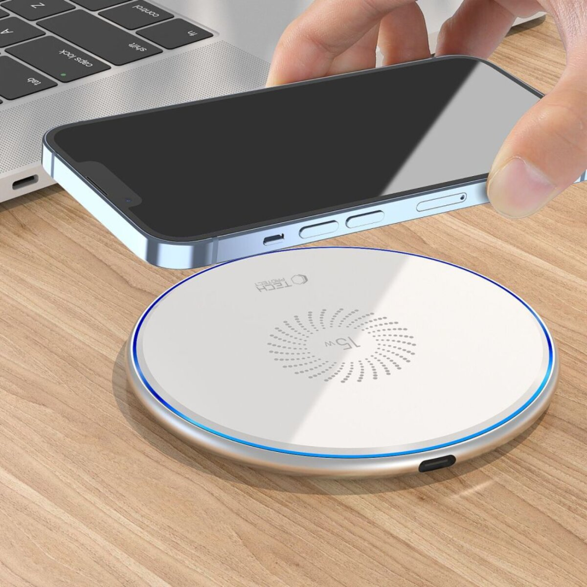 Eine Hand legt ein Smartphone auf ein weißes kabelloses Ladegerät auf einem Holztisch. Im Hintergrund ist ein Laptop.