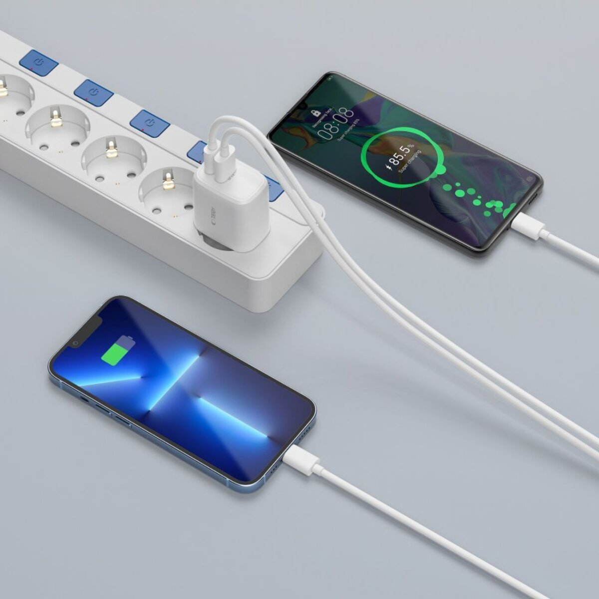 Deux smartphones en charge, connectés à une multiprise. Un chargeur blanc est branché sur la prise, des câbles vont aux téléphones.