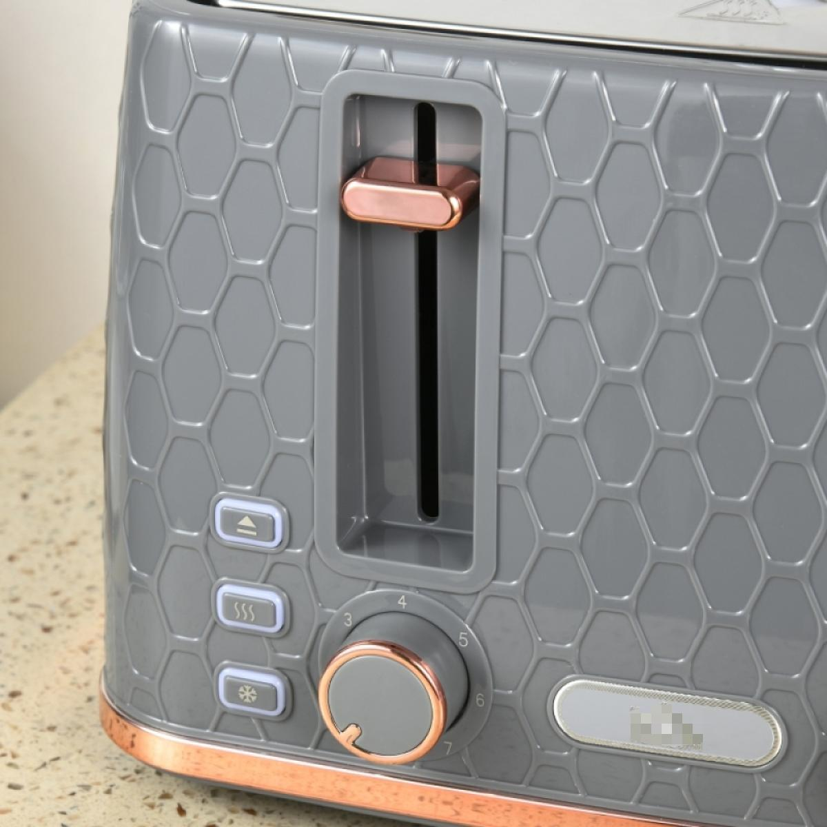Ein grauer Toaster mit Wabenmuster. Er hat roségoldfarbene Akzente, Knöpfe und einen Drehregler. Der Toaster steht auf einer gefleckten Arbeitsplatte.