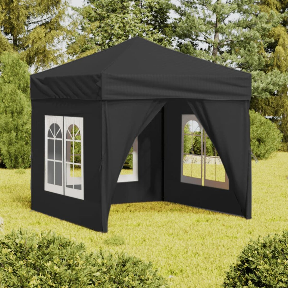 Un gazebo nero con finestre con cornice bianca si trova sull'erba. Alberi sullo sfondo. Cespugli in primo piano.