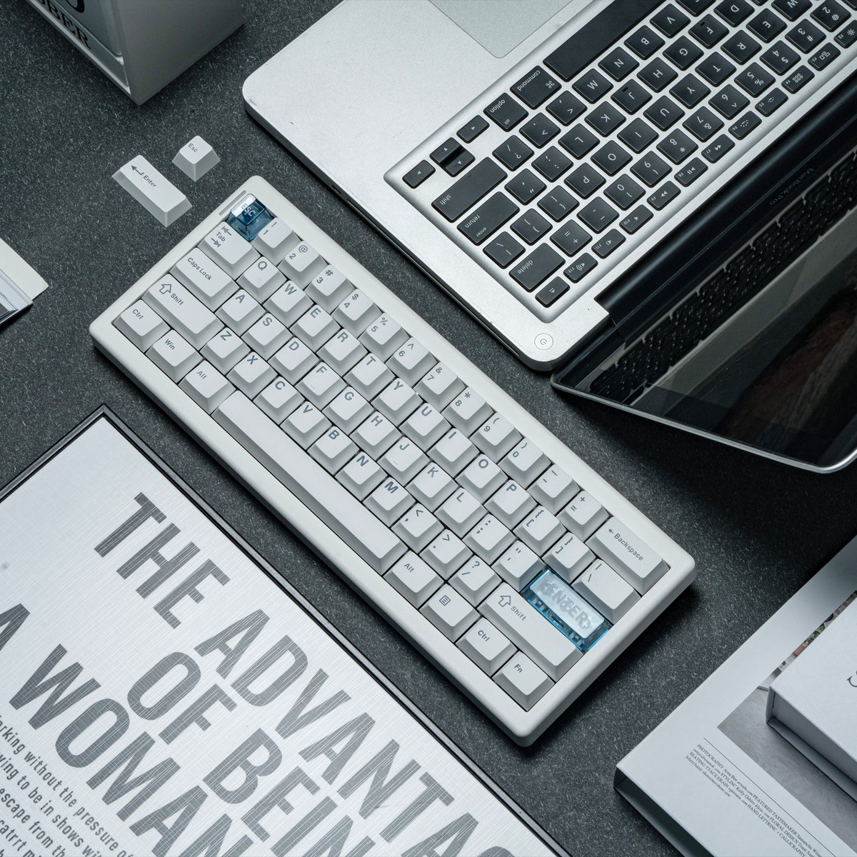 A white keyboard is on a desk with a laptop and printed materials. The keyboard has a blue Enter key.