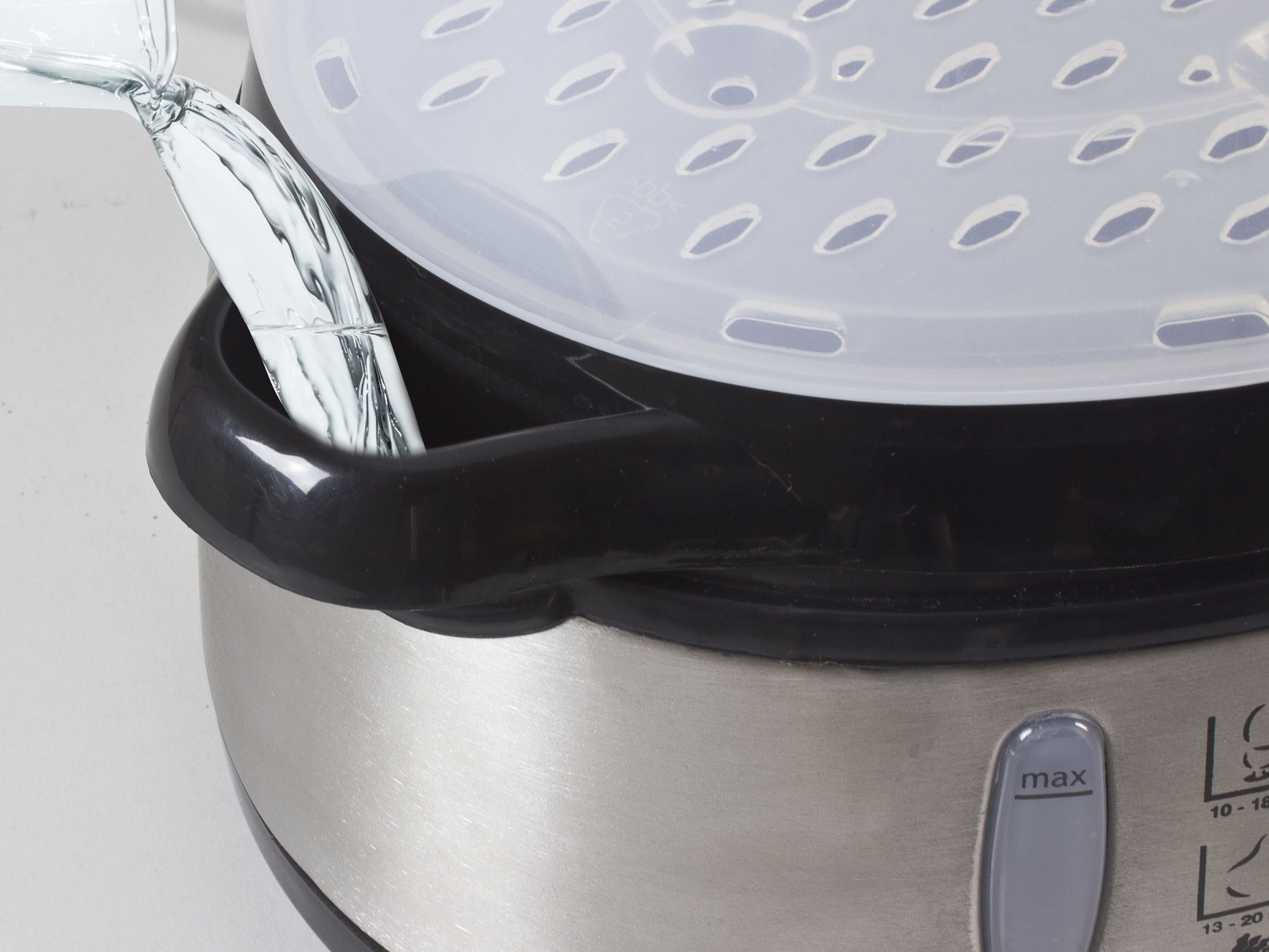 Primo piano di una vaporiera in acciaio inossidabile con acqua versata. Il coperchio ha fori ovali.