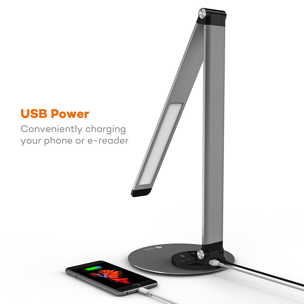 Eine moderne Schreibtischlampe mit Smartphone-Ladung. Die Lampe ist grau und silber. Das Telefon ist schwarz und lädt. Der Hintergrund ist weiß.