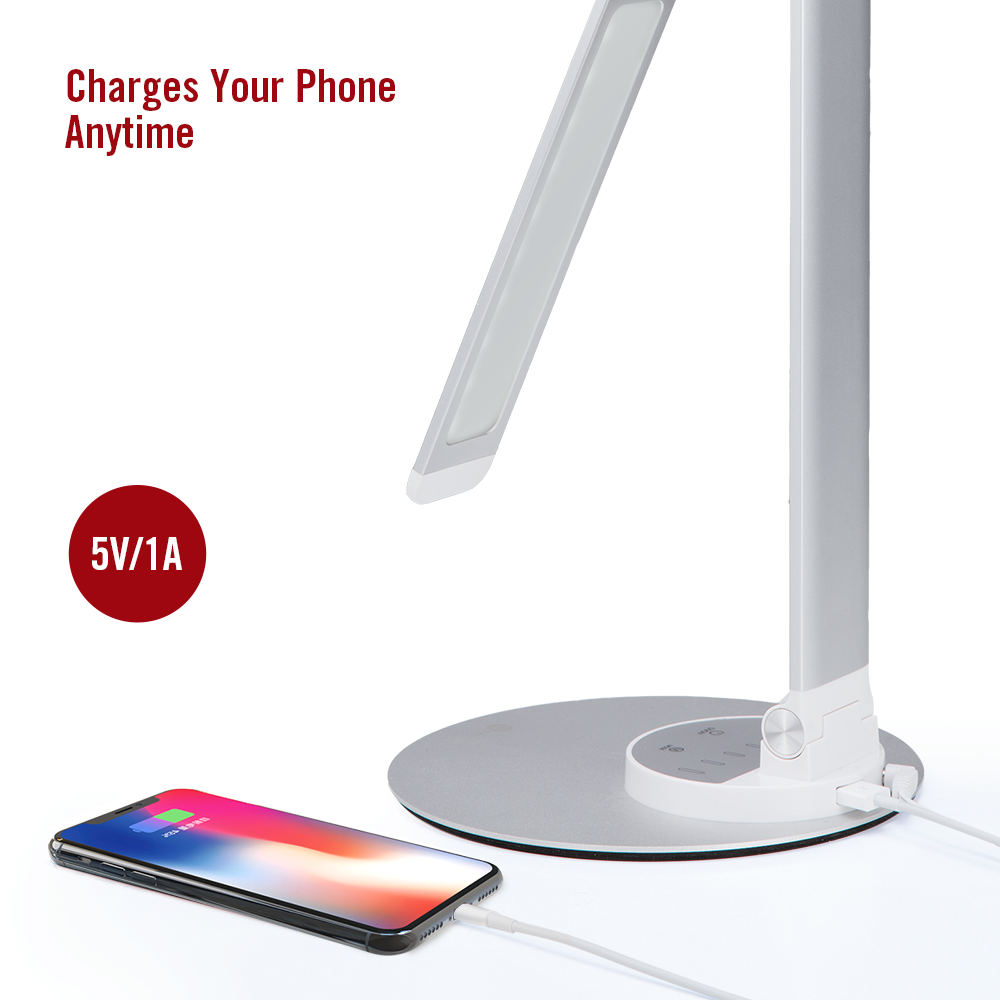 Eine Schreibtischlampe mit einem Telefon, das auf einer weißen Oberfläche geladen wird. Die Lampe ist silber und weiß.