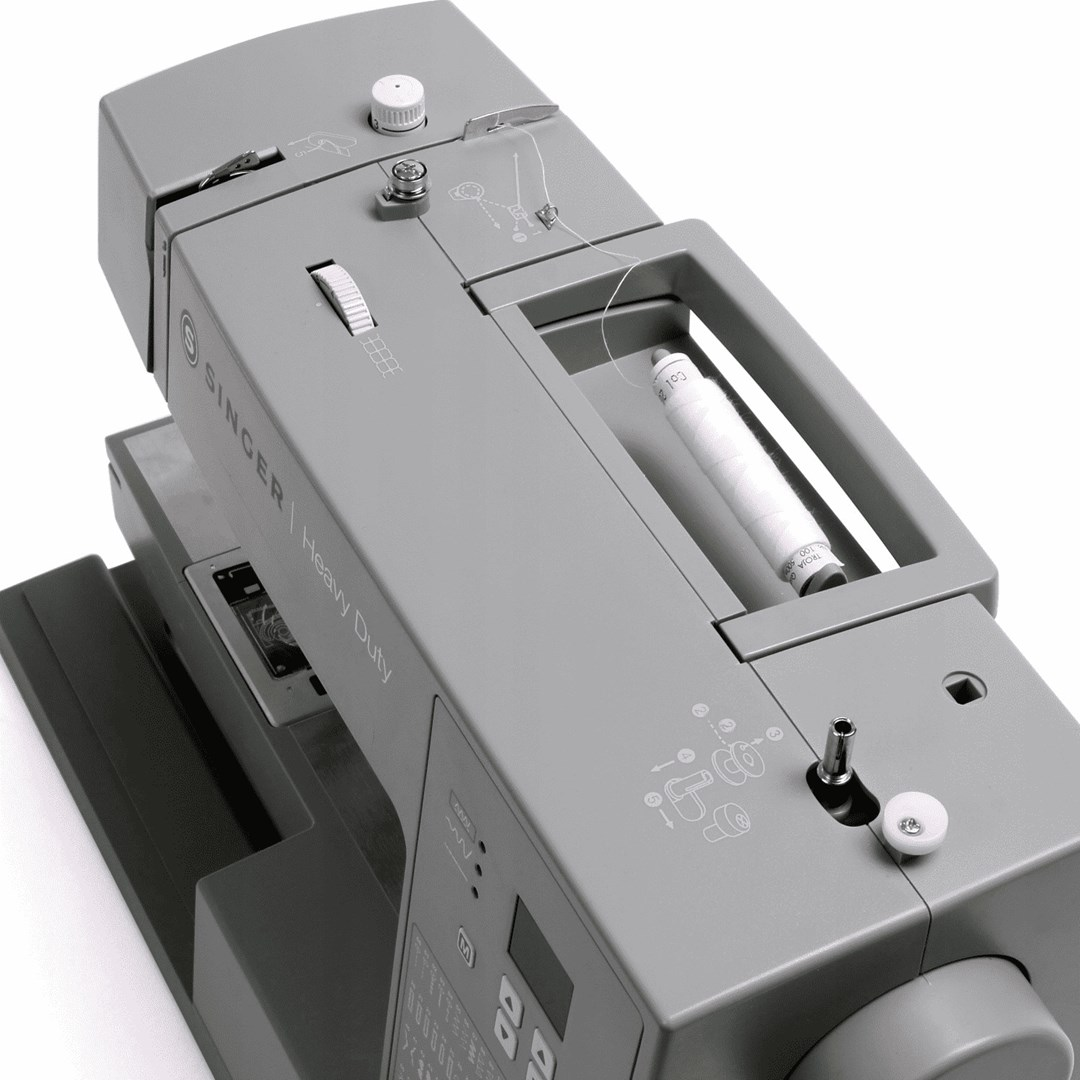 Szara maszyna do szycia Singer Heavy Duty. Posiada szpulkę białej nici, panel sterowania oraz różne pokrętła i przyciski.