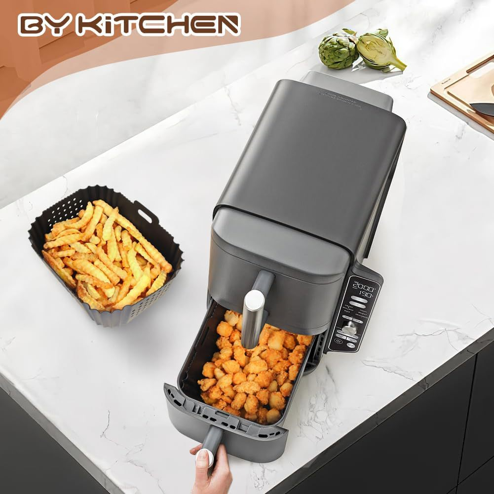 Eine Heißluftfritteuse mit Pommes und Frittiertem. Eine Hand zieht den Korb heraus. Artischocken im Hintergrund.