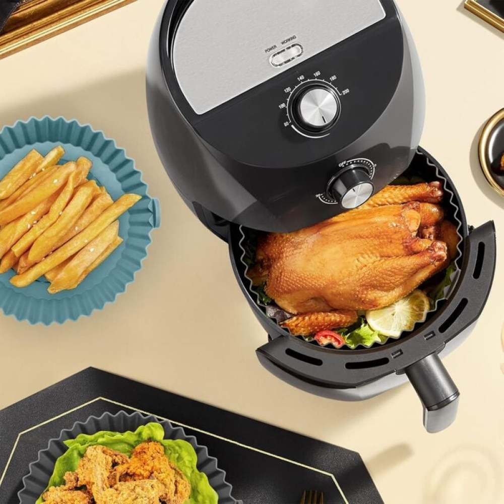 Eine Heißluftfritteuse mit einem gebratenen Hähnchen, Pommes Frites in einem blauen Gericht und frittiertem Essen in einem schwarzen Gericht.