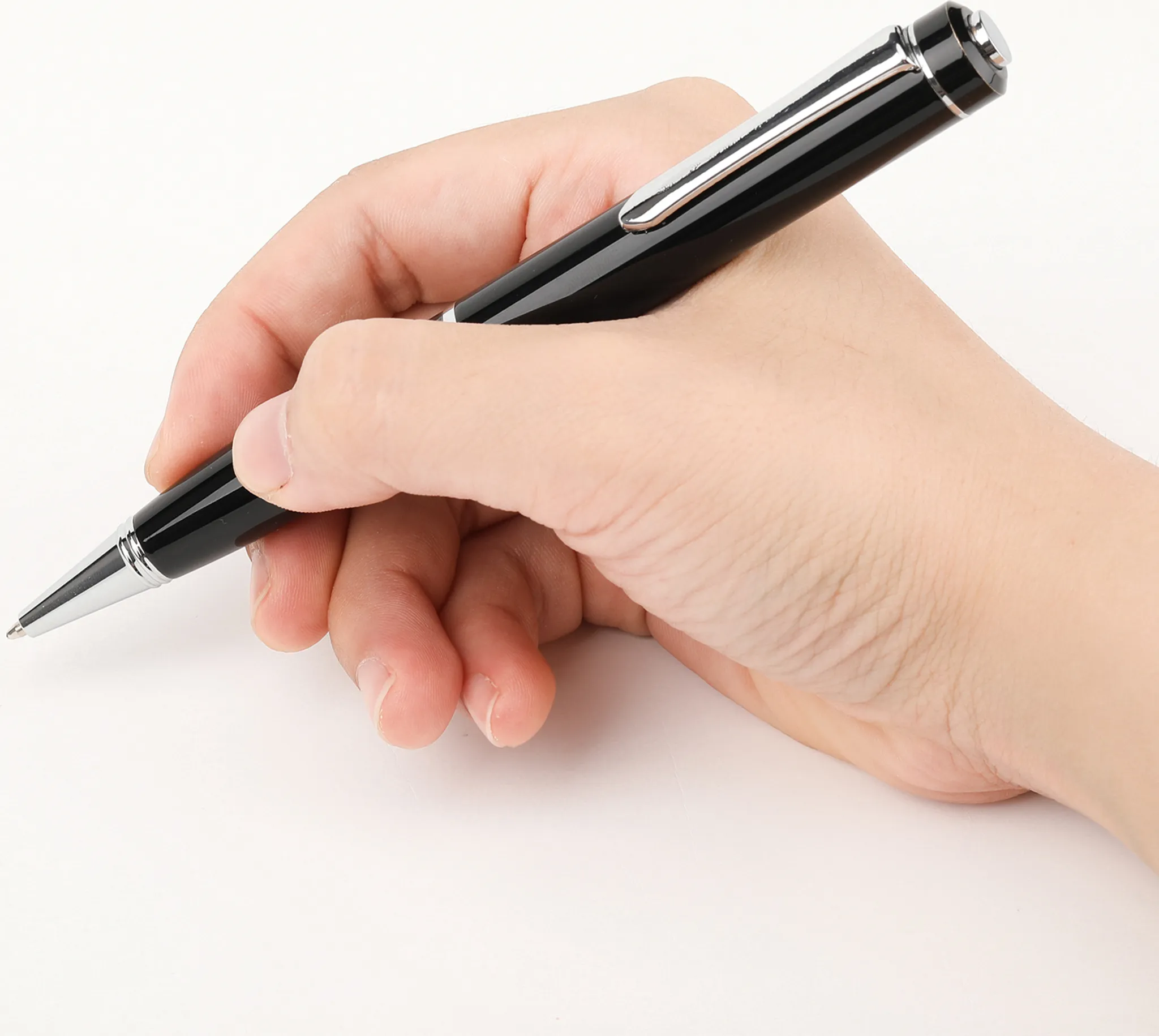Eine Hand hält einen schwarzen Stift mit silbernem Clip und schreibt auf eine weiße Oberfläche. Der Stift ist abgewinkelt.