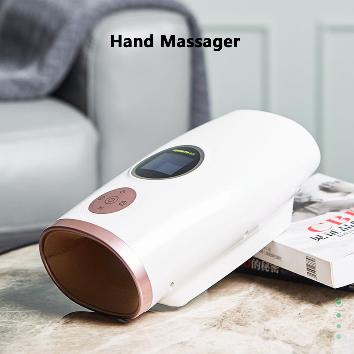 Ein weißes Handmassagegerät mit Bildschirm und Knöpfen liegt auf einer Marmoroberfläche. Im Hintergrund sind ein Buch und ein Sofa zu sehen.