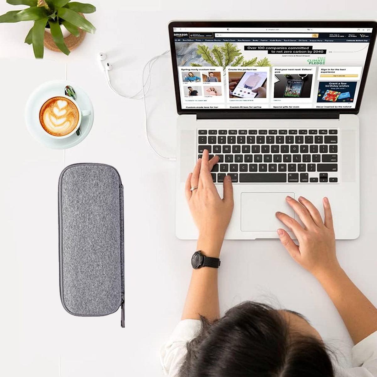Eine Person benutzt einen Laptop. Eine Tasse Kaffee, ein Federmäppchen und Kopfhörer liegen auf dem Tisch. Der Laptop zeigt Amazon.