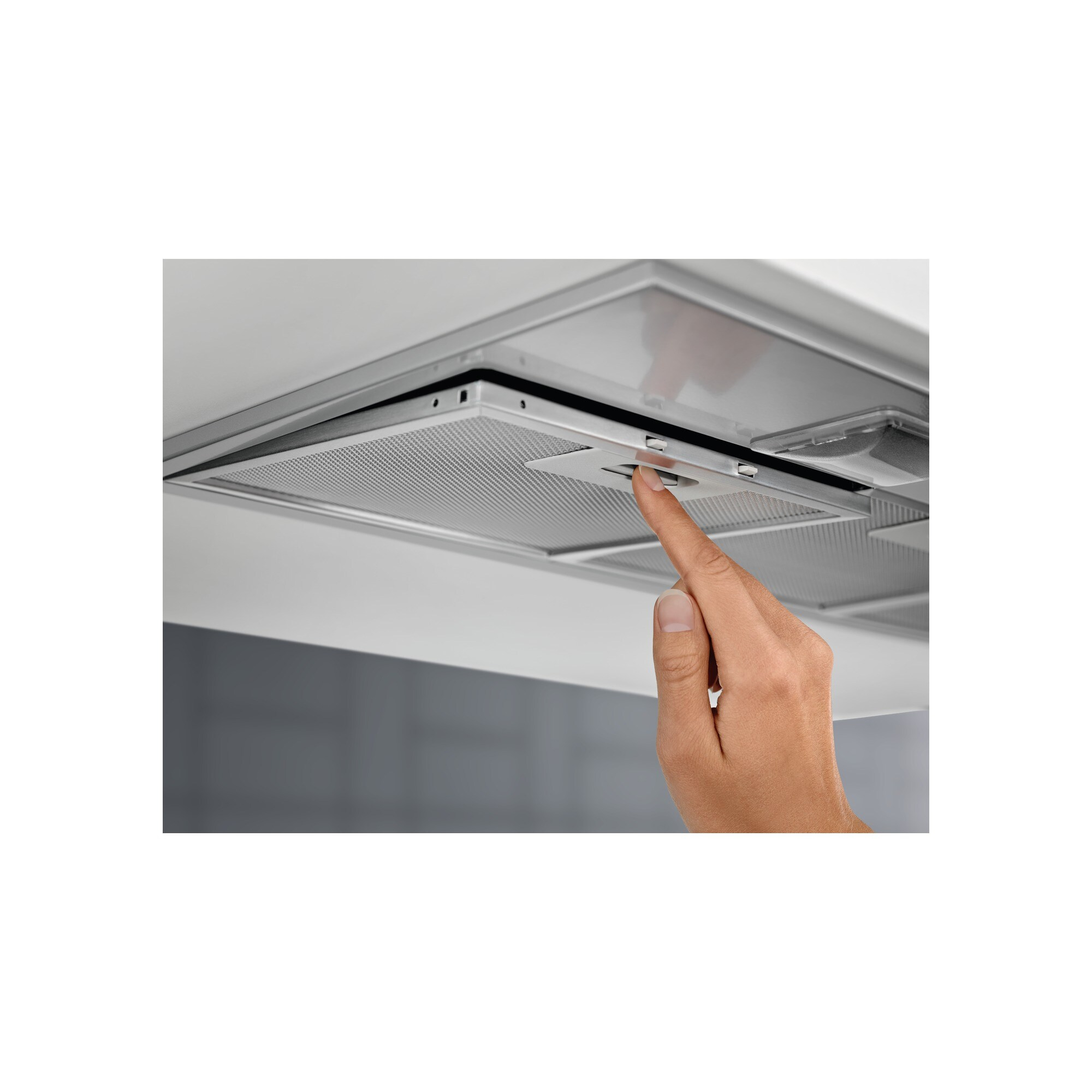 Una mano preme un pulsante su una cappa d'argento. Lo sfondo mostra un soffitto bianco e un muro grigio.