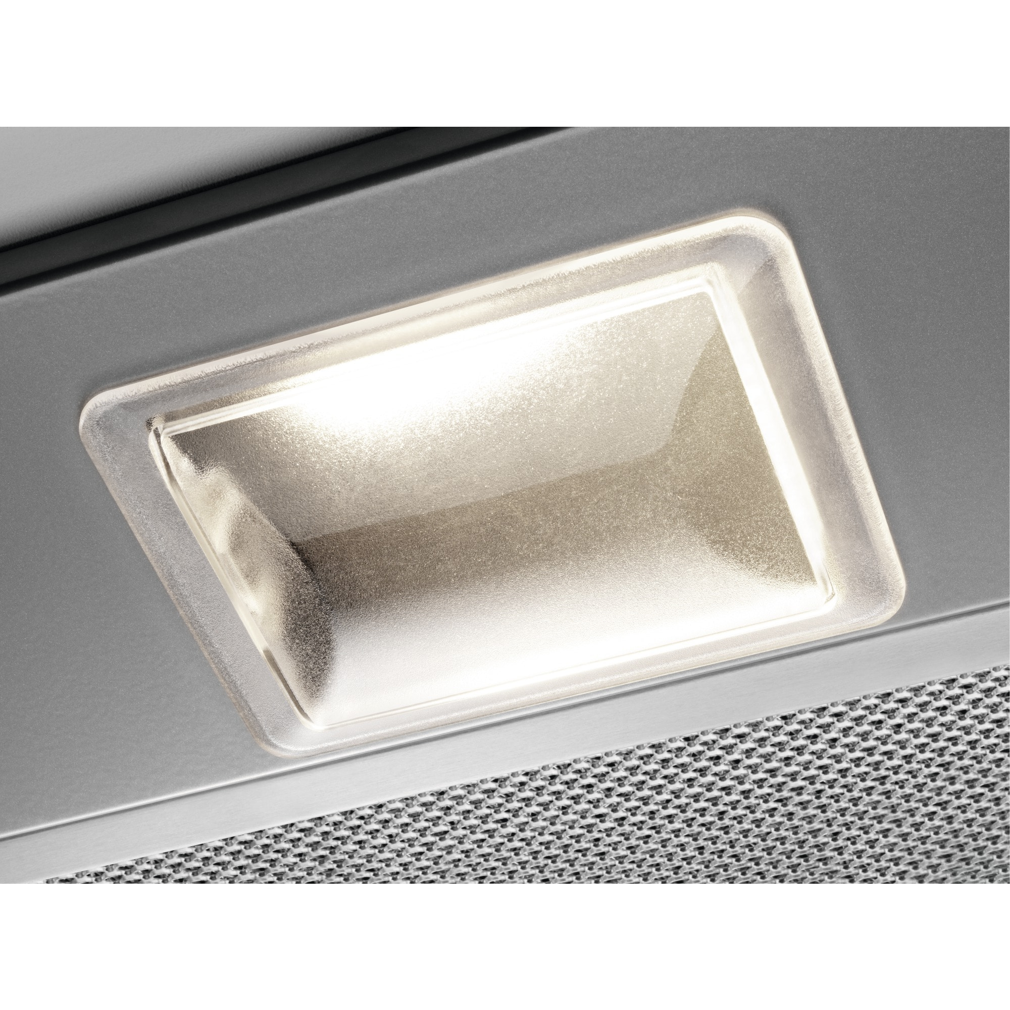 Primo piano di una luce della cappa della cucina. È rettangolare, luminosa e inserita in un pannello argentato sopra una rete metallica.