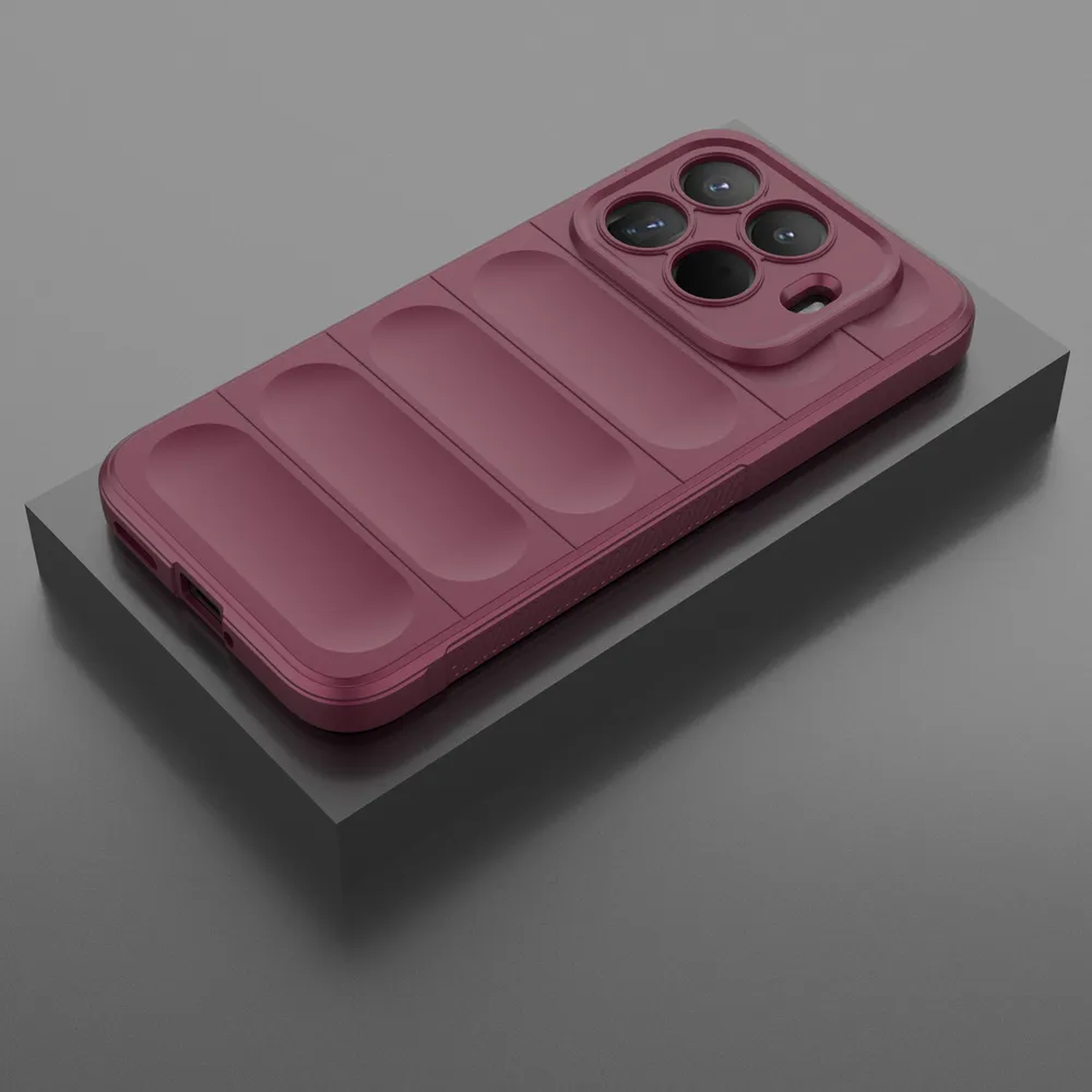 Een bordeauxrode telefoonhoes met lensafdekking ligt op een grijs blok. De hoes heeft een gestructureerd rugontwerp en een uitsparing voor de camera.