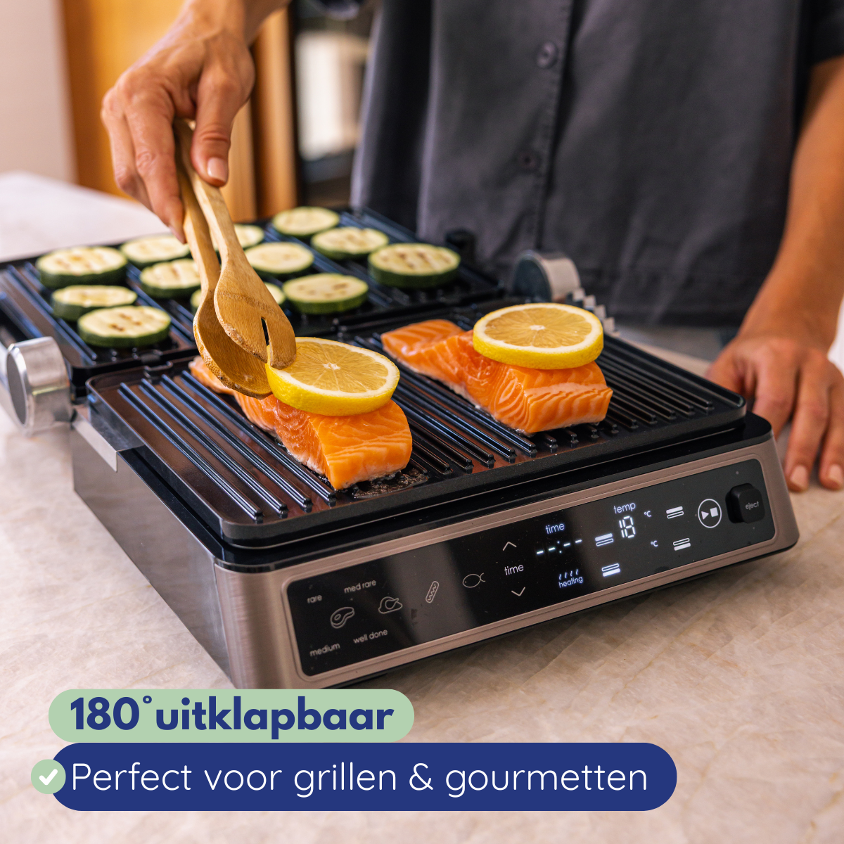 A person grilling salmon with lemon slices and zucchini on an electric grill. Wooden utensils are used. The grill is on.