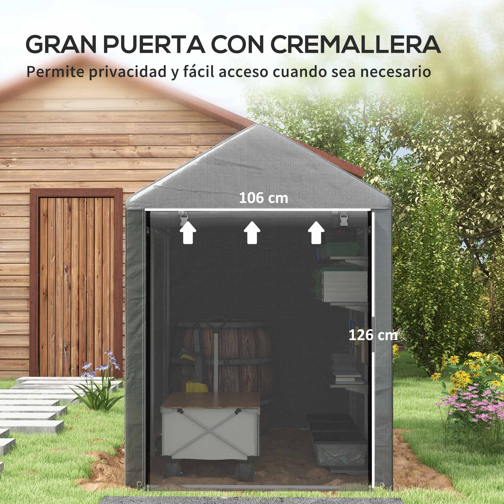 Un cobertizo gris con puerta con cremallera está en un área cubierta de hierba. El cobertizo tiene una puerta de madera. Flores y árboles están detrás.