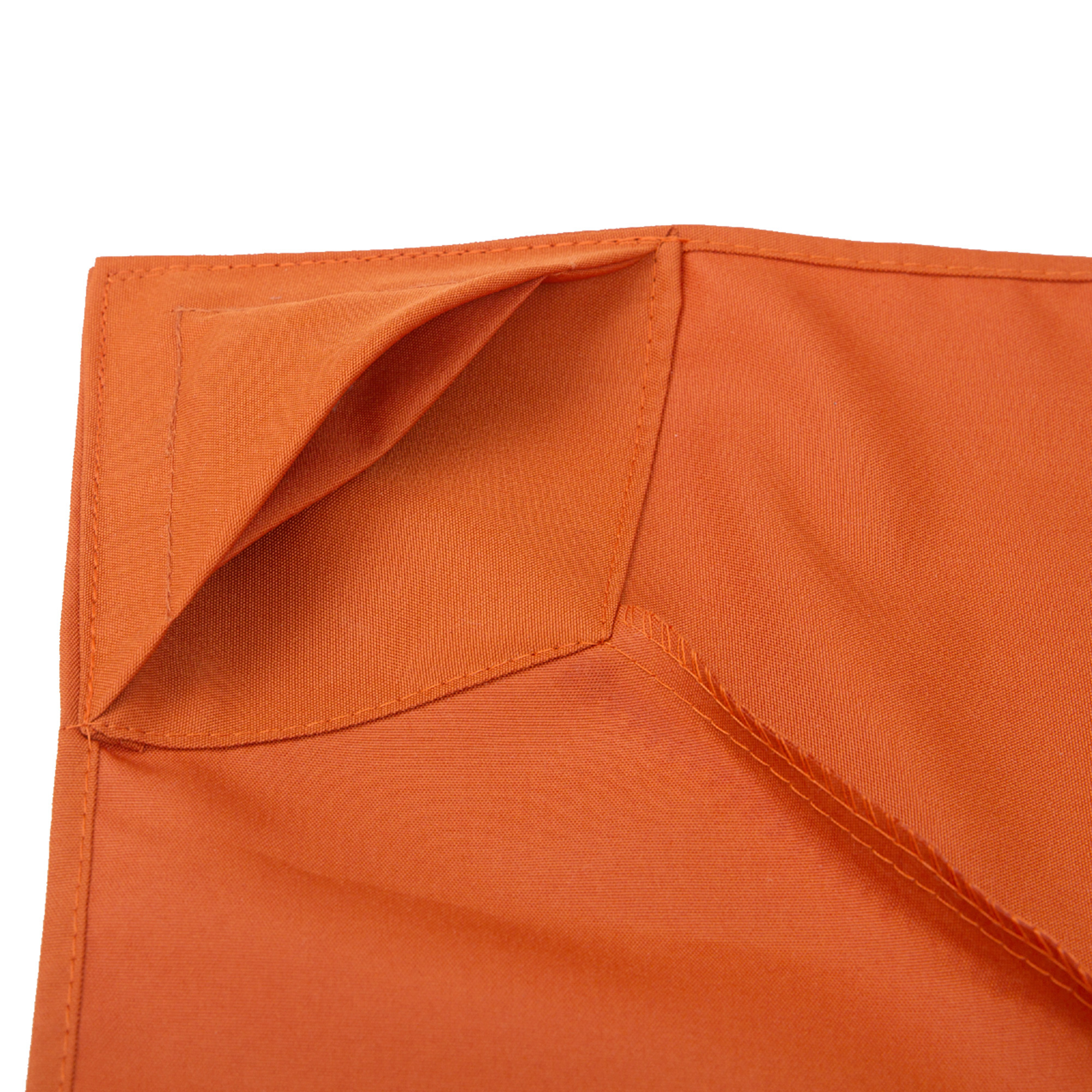 Primer plano de una esquina de tela naranja. Costuras visibles y un detalle plegado en forma de bolsillo. Fondo blanco.