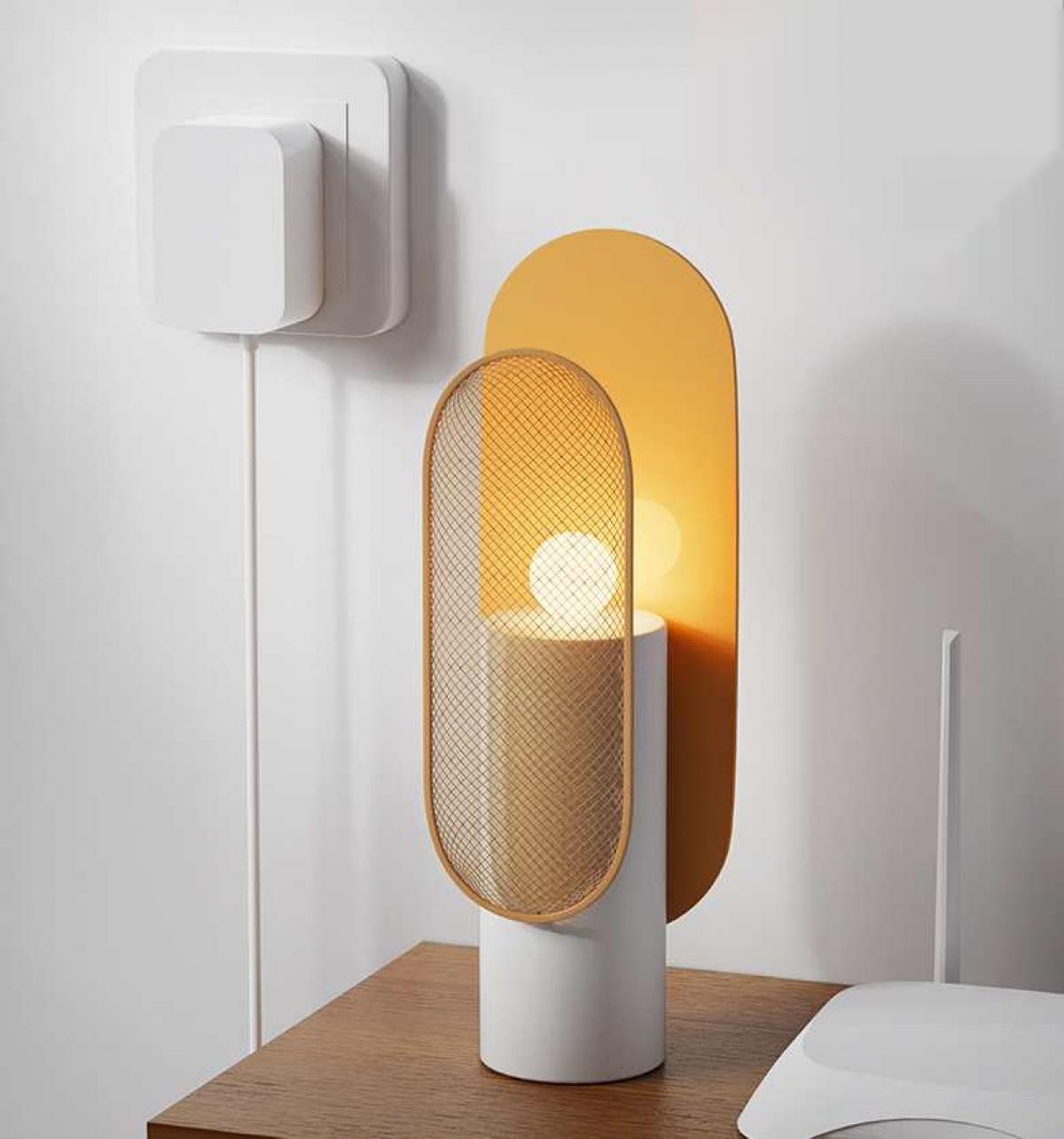 Eine moderne Lampe mit gelbem und goldenem Design steht auf einem Holztisch. Ein weißer Stecker und Router sind ebenfalls sichtbar.