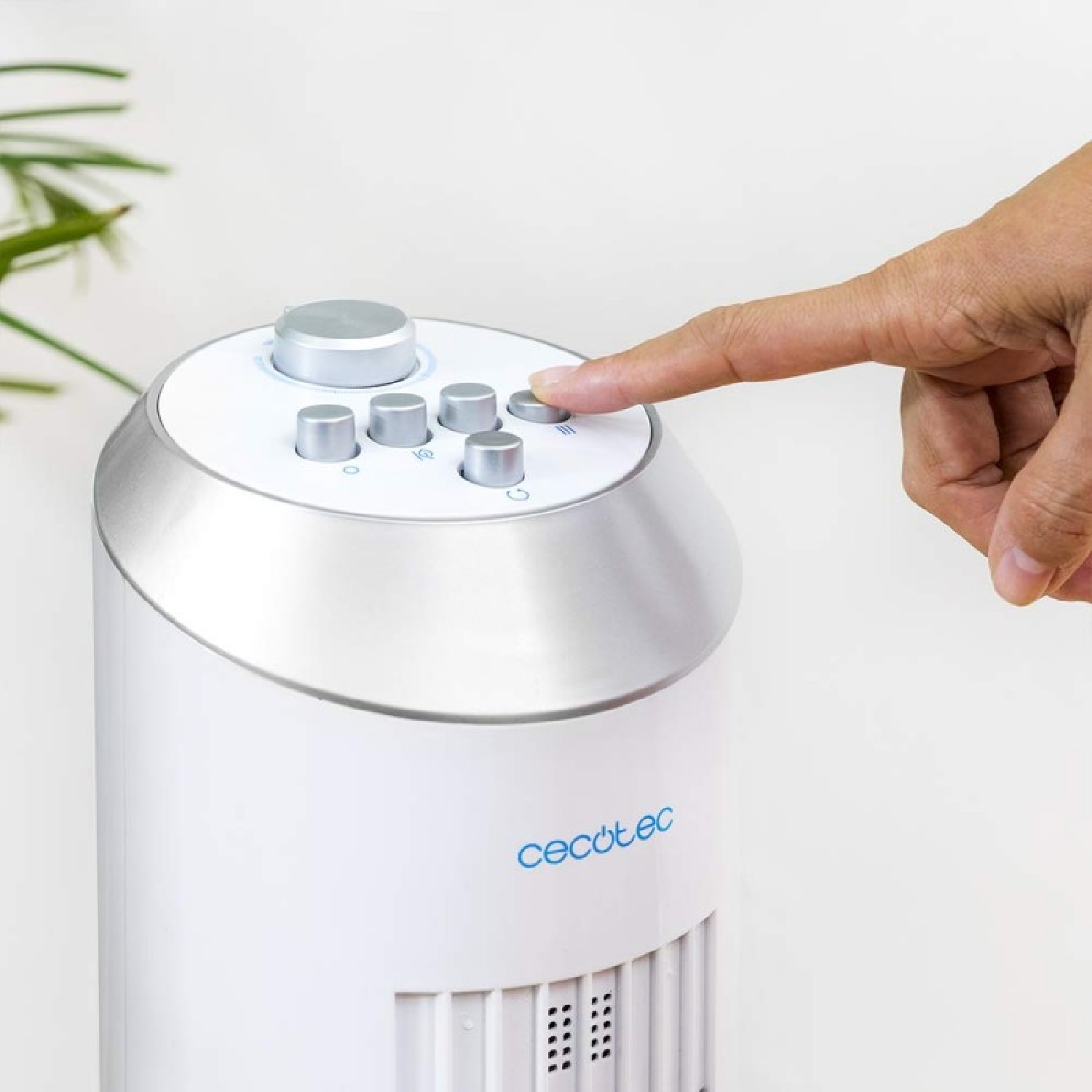 Ręka naciska przycisk na białym wentylatorze. Wentylator ma srebrne akcenty i panel sterowania.