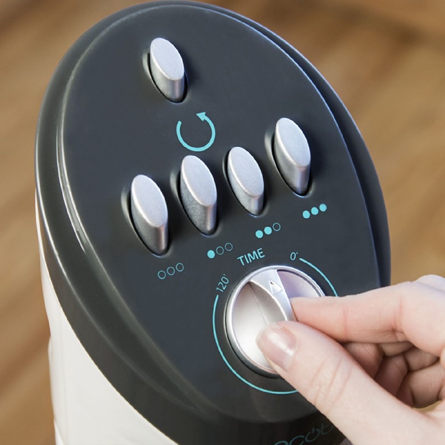 Ręka reguluje pokrętło timera na czarnym panelu sterowania urządzenia. Widoczne są srebrne przyciski i wskaźnik czasu.