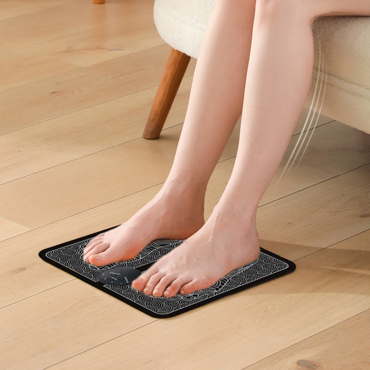 Barfuß auf einer Fußmassage-Matte. Beine sind sichtbar, zusammen mit einem Stuhl und Holzboden. Die Matte ist schwarz mit weißen Designs.