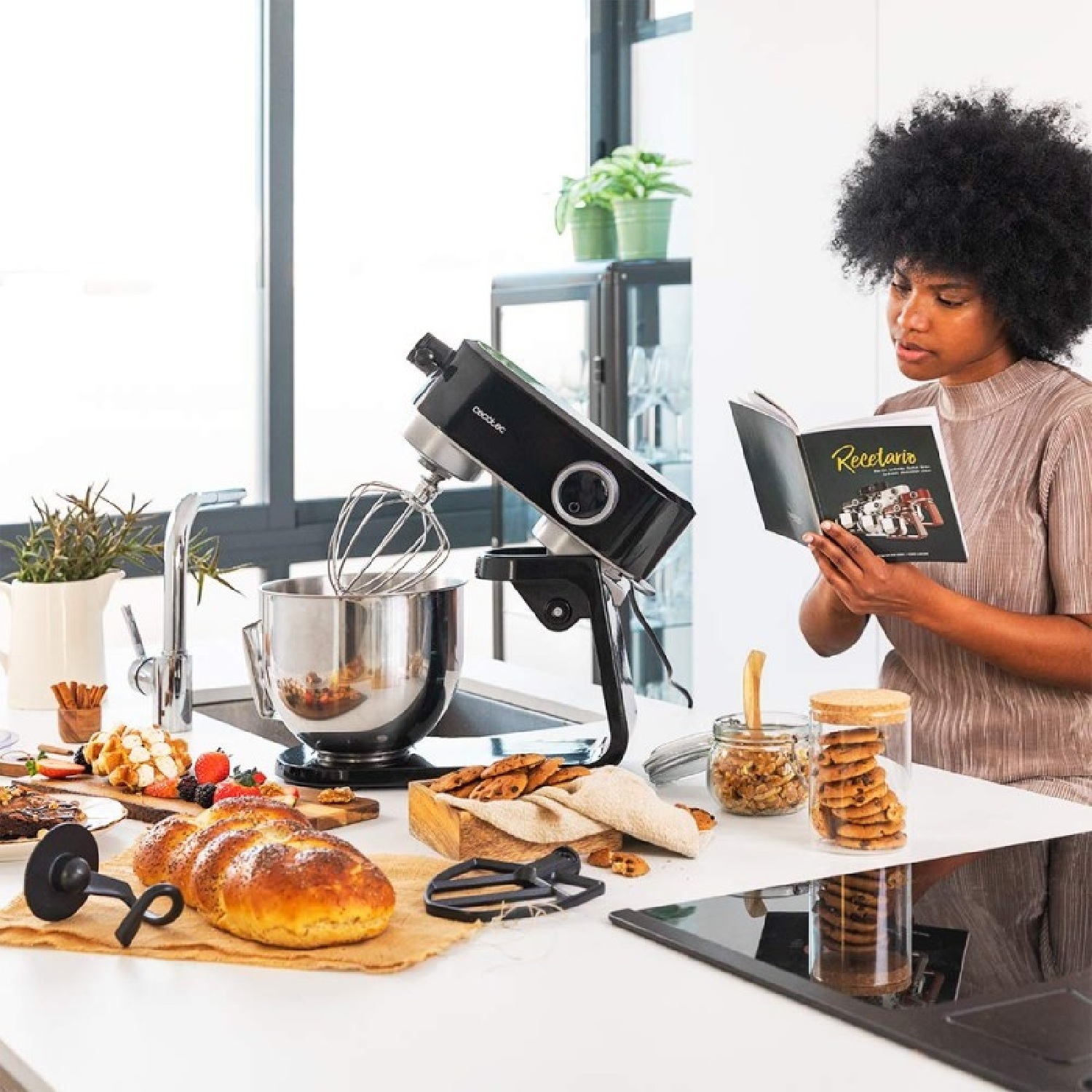 Donna legge libro di cucina vicino a mixer, pane, biscotti e frutta. Scena di cucina con ingredienti.