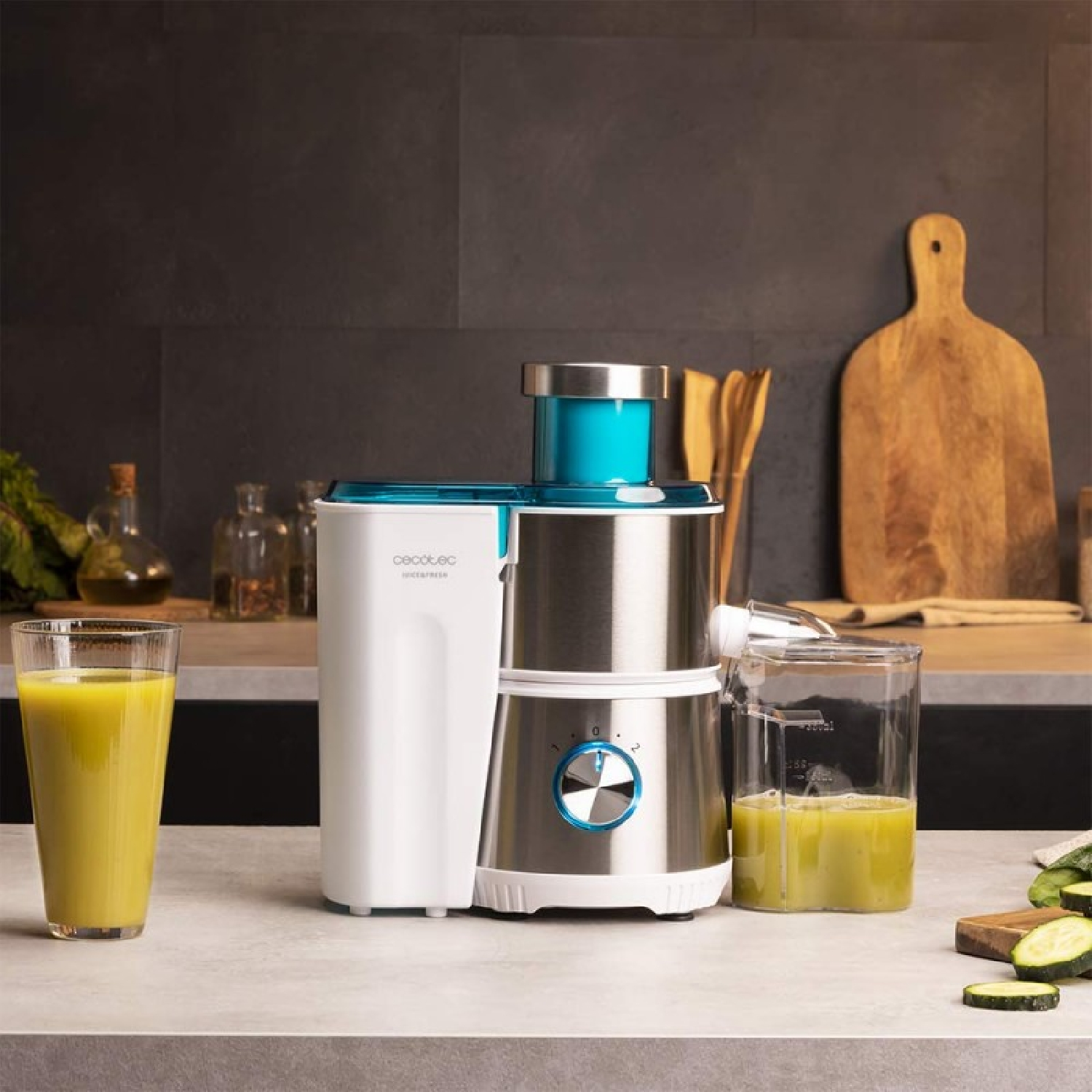 Una centrifuga con bicchieri di succo, un tagliere e zucchine. La centrifuga è bianca e argentata.