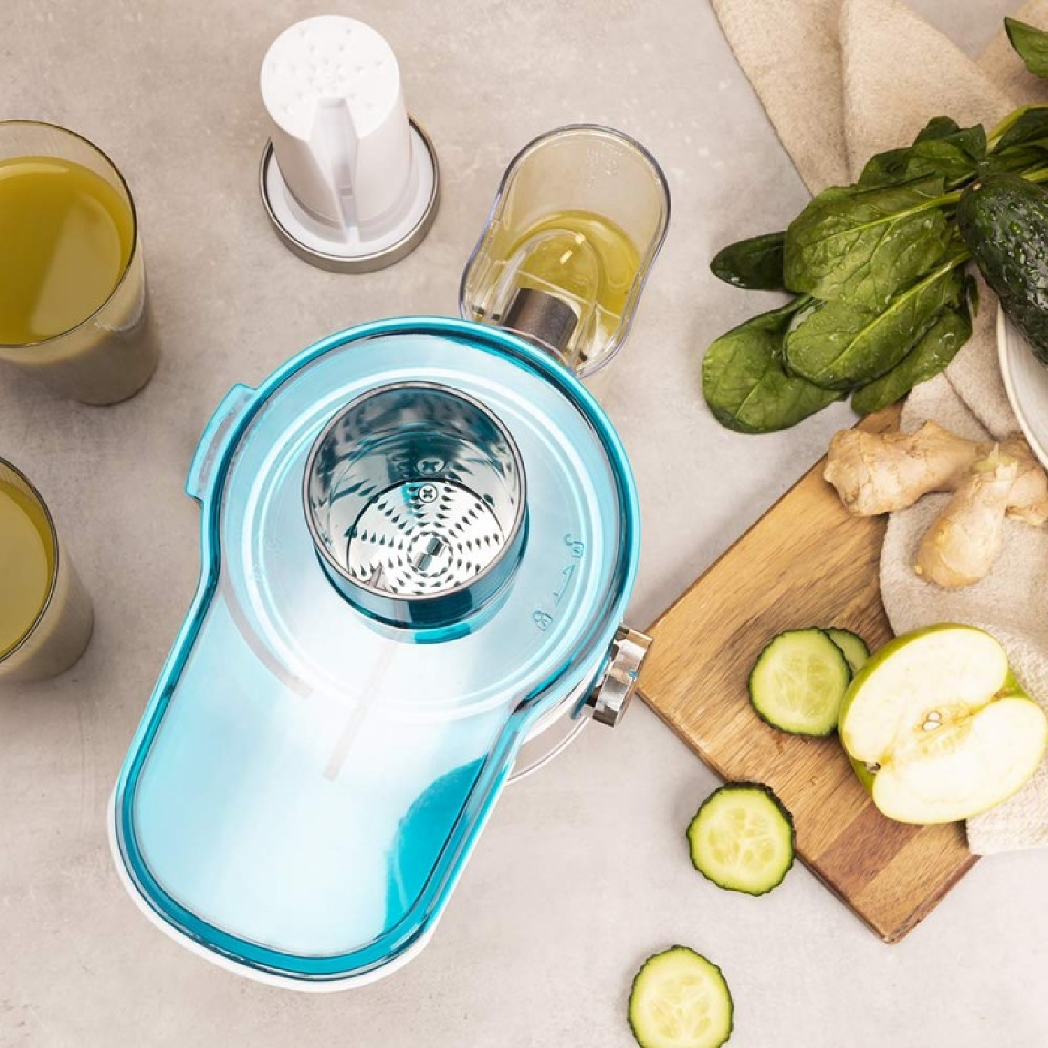 Un estrattore di succo con ingredienti come spinaci, cetrioli e mele. Sono visibili bicchieri di succo. L'estrattore è blu.