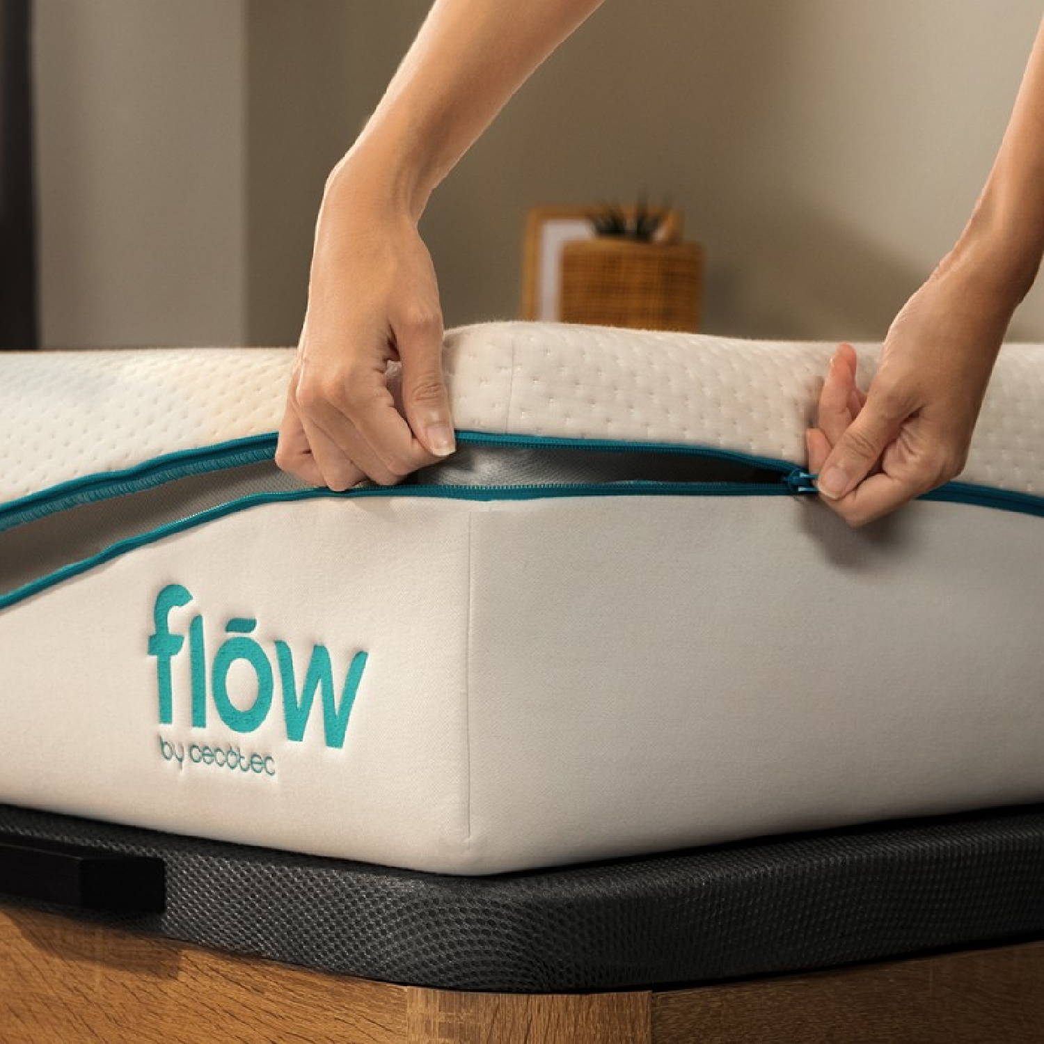 Mani che chiudono con la cerniera un materasso bianco con cerniera turchese. Il materasso ha la parola 'flow' in turchese. Sfondo: struttura in legno.