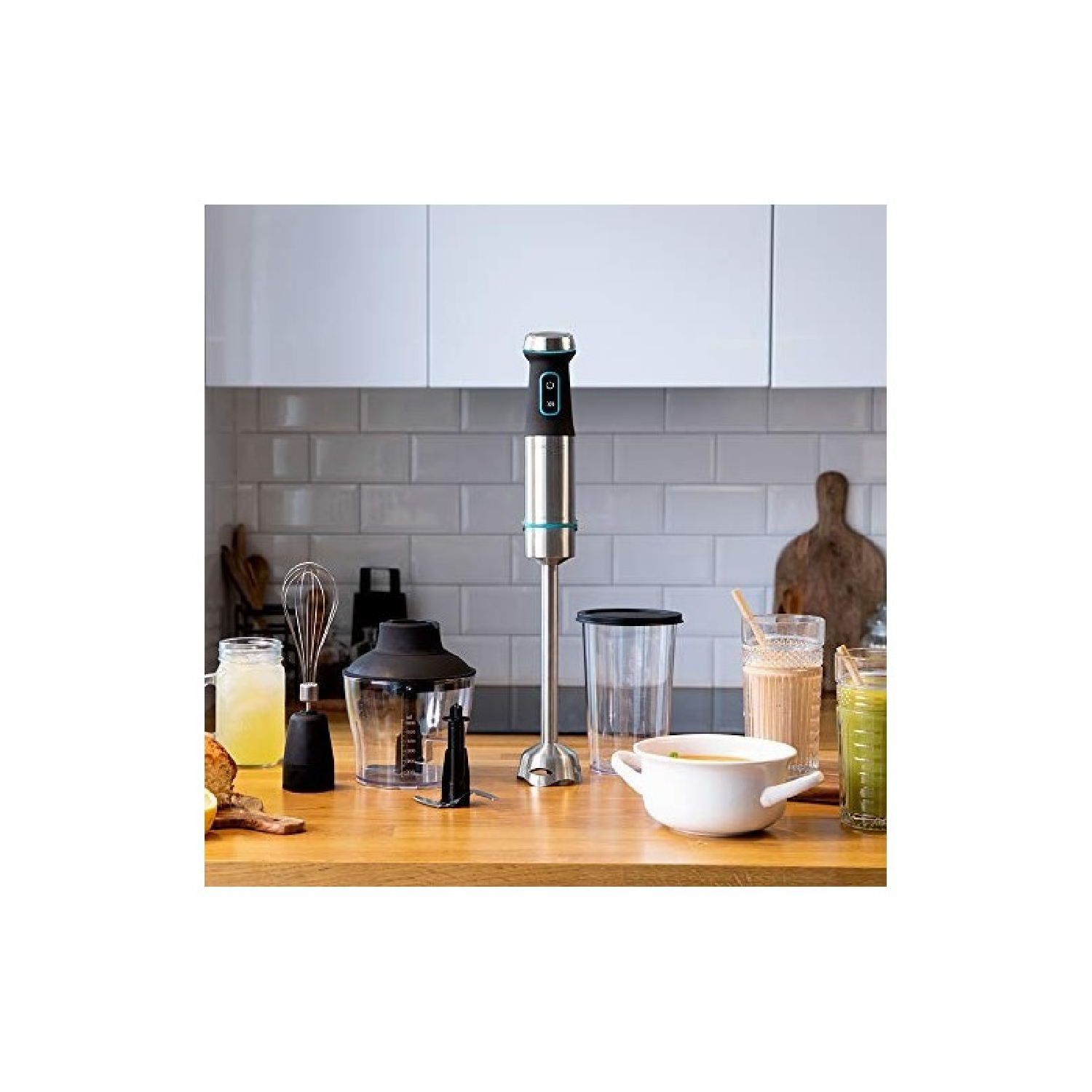 Keuken met een blender, glazen en kommen op een houten oppervlak. Witte kasten en betegelde muur op de achtergrond.