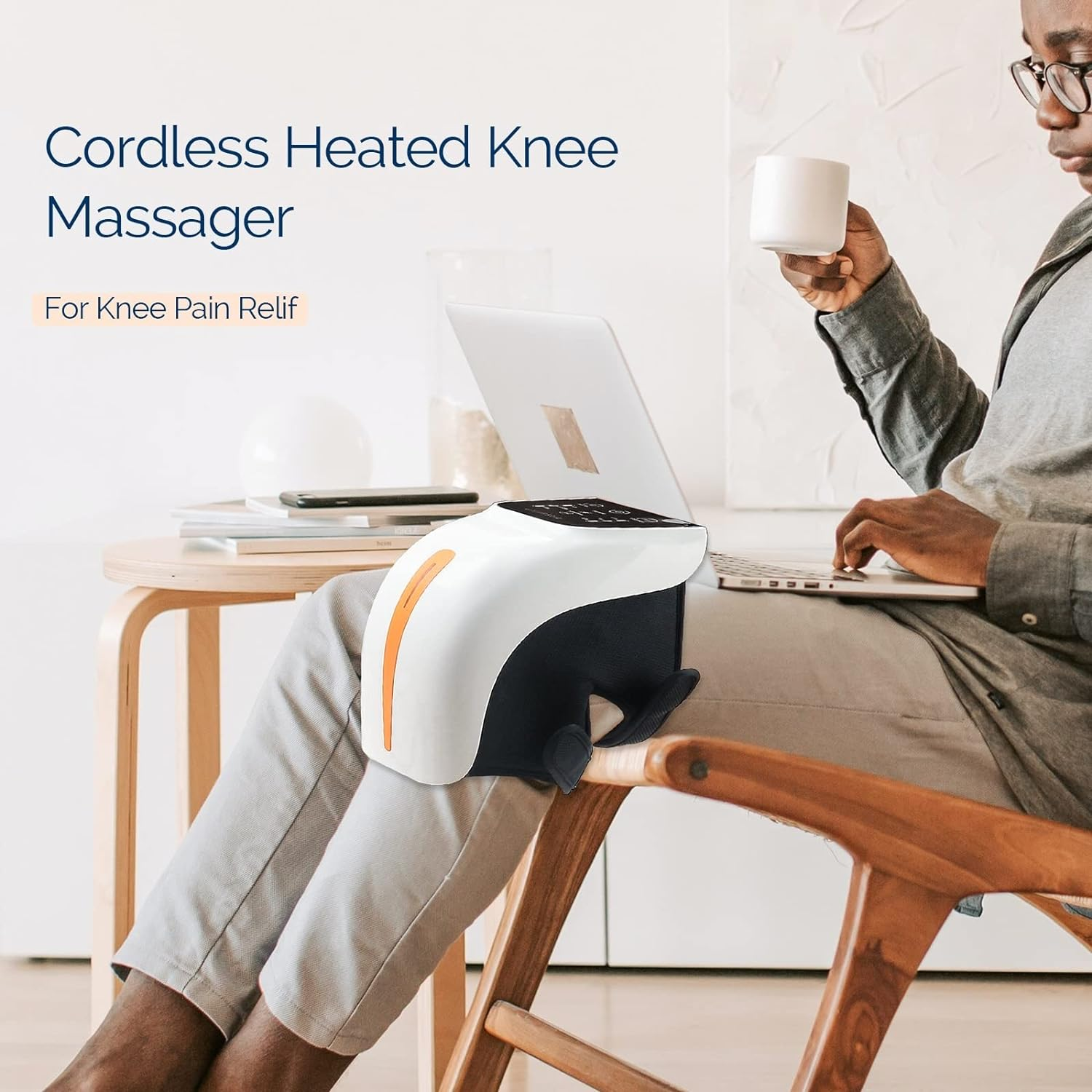 Ein Mann benutzt einen Laptop, während er eine Tasse hält. Ein Kniemassagegerät liegt auf seinem Knie. Text: Kabelloser beheizter Kniemassager.