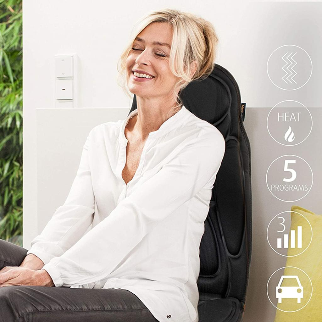 Eine Frau lächelt auf einem Massagestuhl. Sie trägt ein weißes Hemd und graue Hose. Symbole für Wärme, Programme und Auto sind sichtbar.