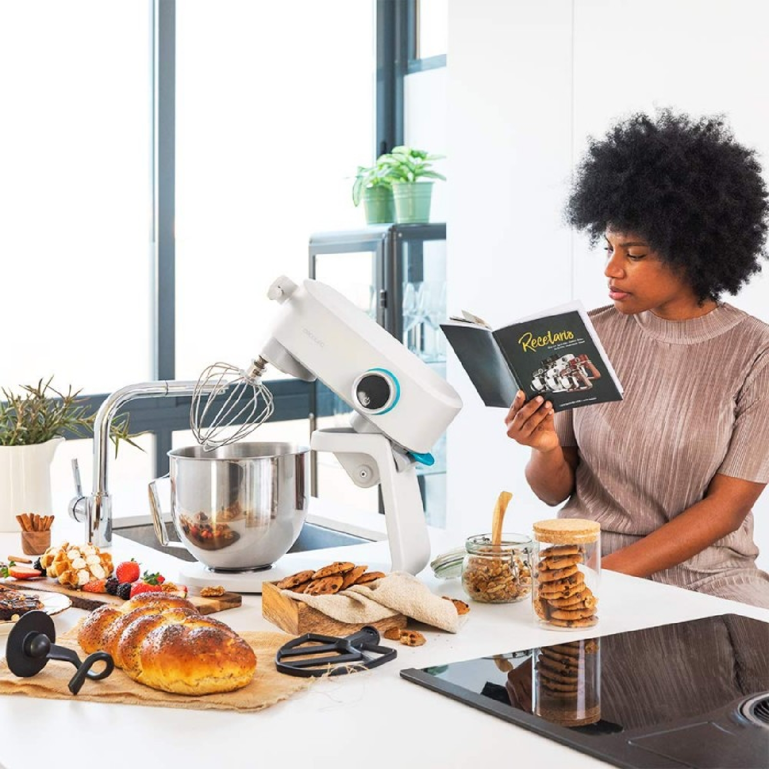 Una donna legge un libro di cucina in cucina. Un mixer, prodotti da forno e ingredienti sono sul bancone.