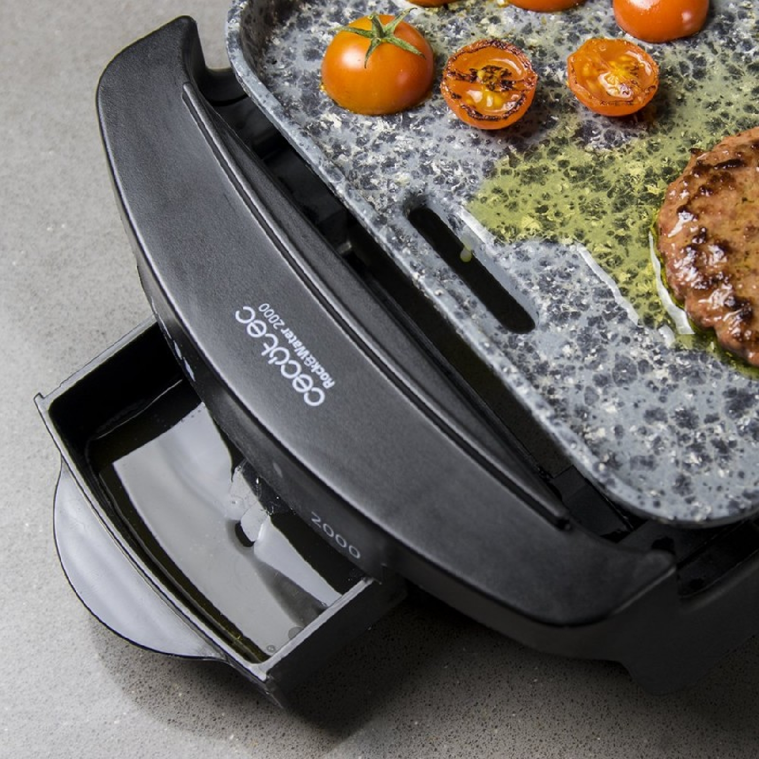 Zbliżenie czarnego grilla z pomidorami i smażącym się burgerem. Widoczny olej. Grill ma funkcję wody.