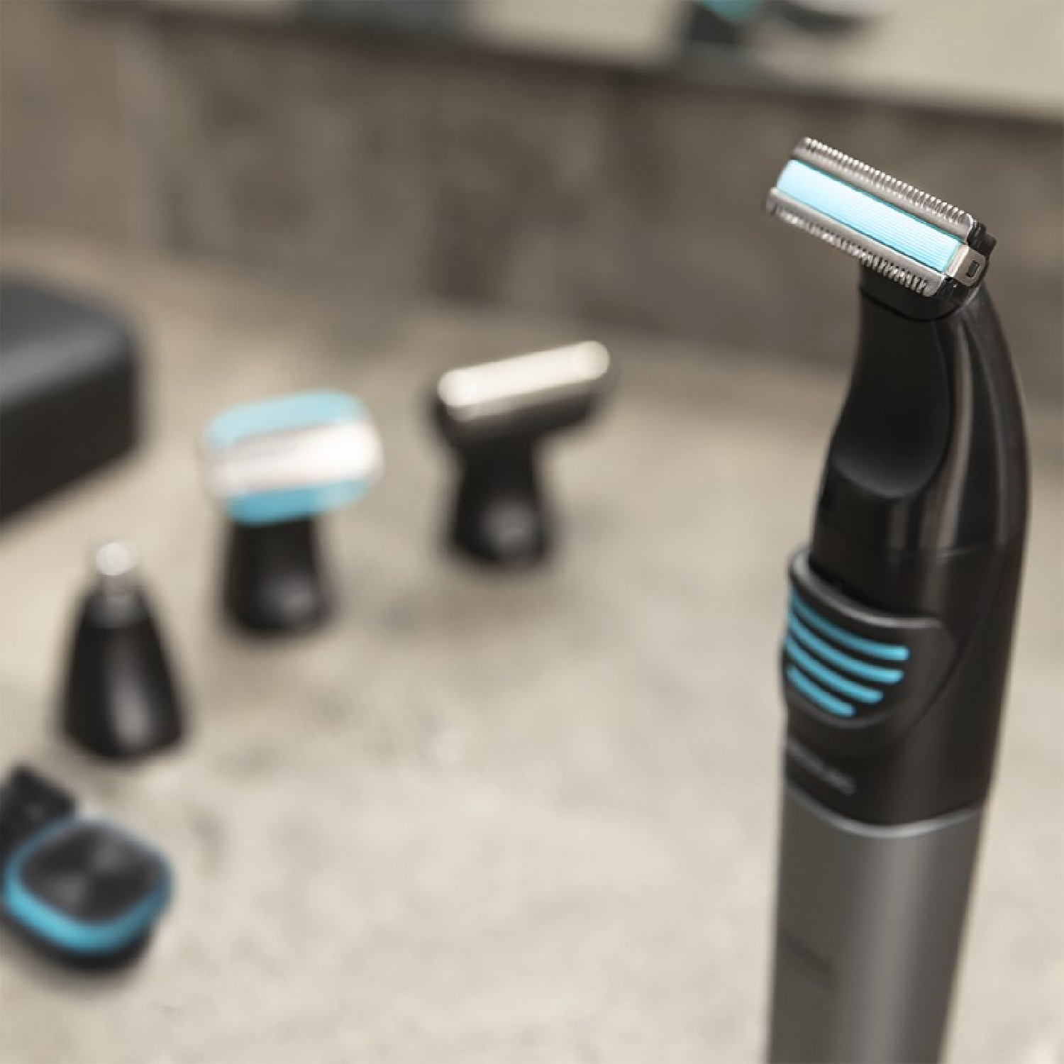 Primer plano de una afeitadora eléctrica negra y plateada con detalles azules. Varios accesorios borrosos en el fondo.