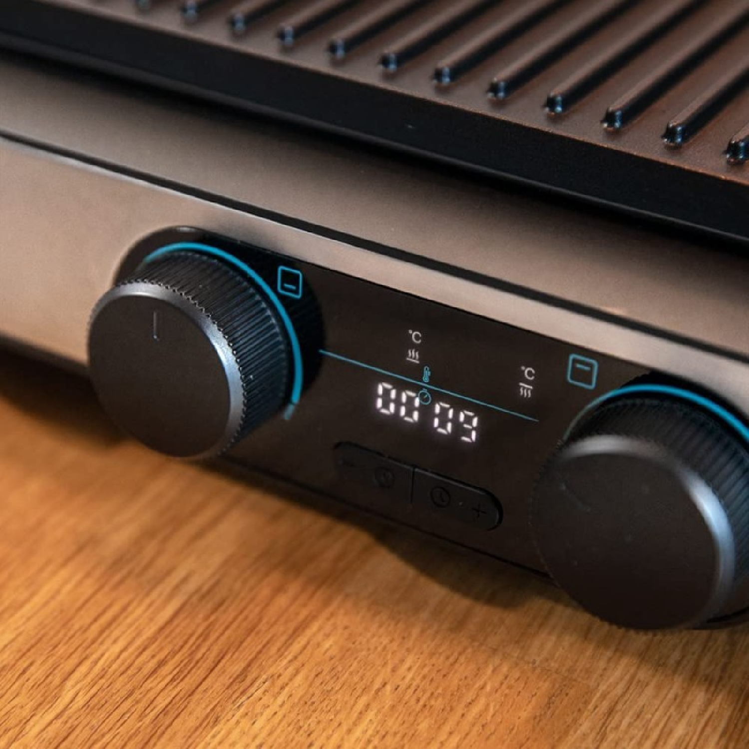 Primo piano di una griglia con manopole di controllo e un display digitale che mostra '00:09'. La griglia è su una superficie di legno.