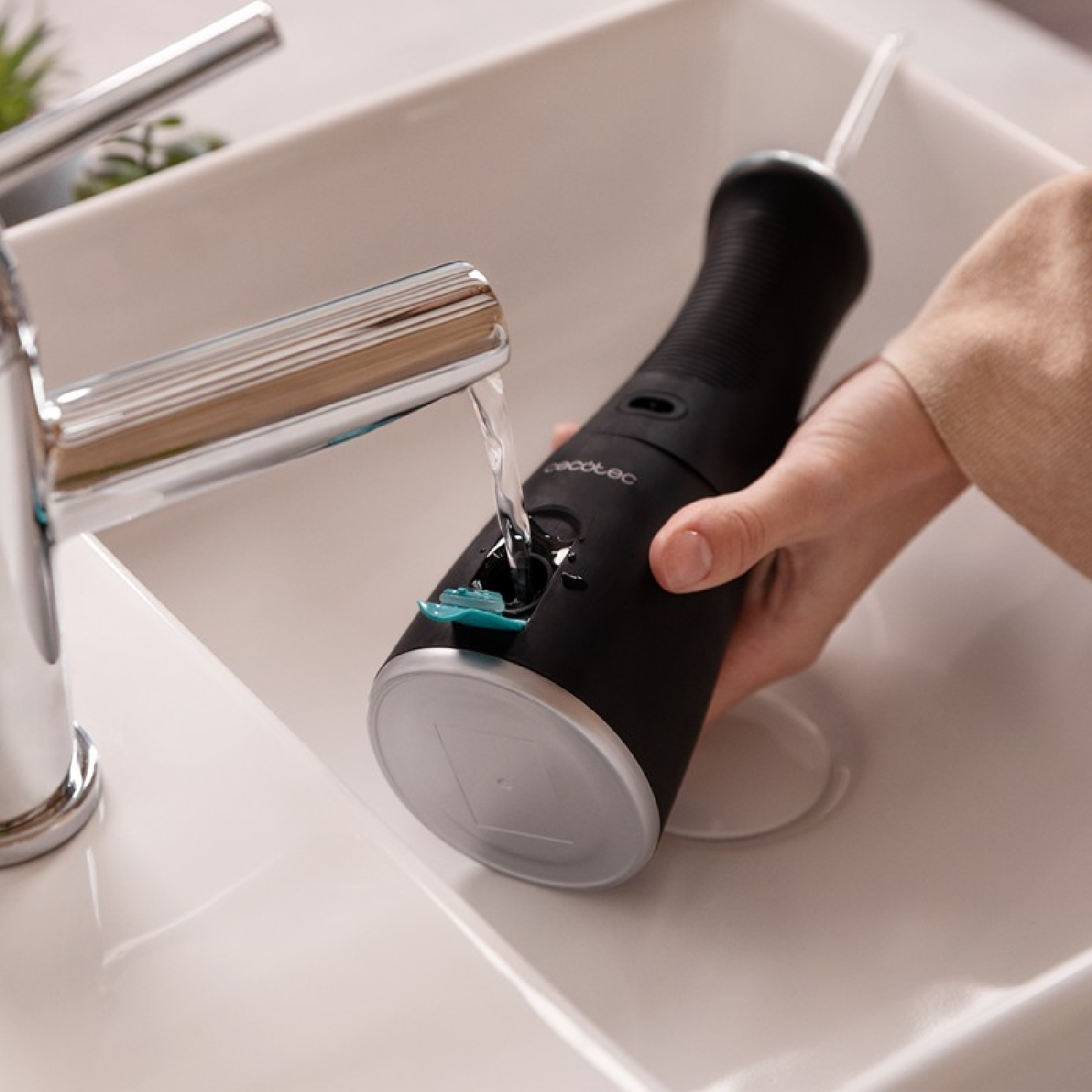 Osoba napełnia czarny irygator wodą z chromowanej baterii w białej umywalce. Podstawa jest szara.