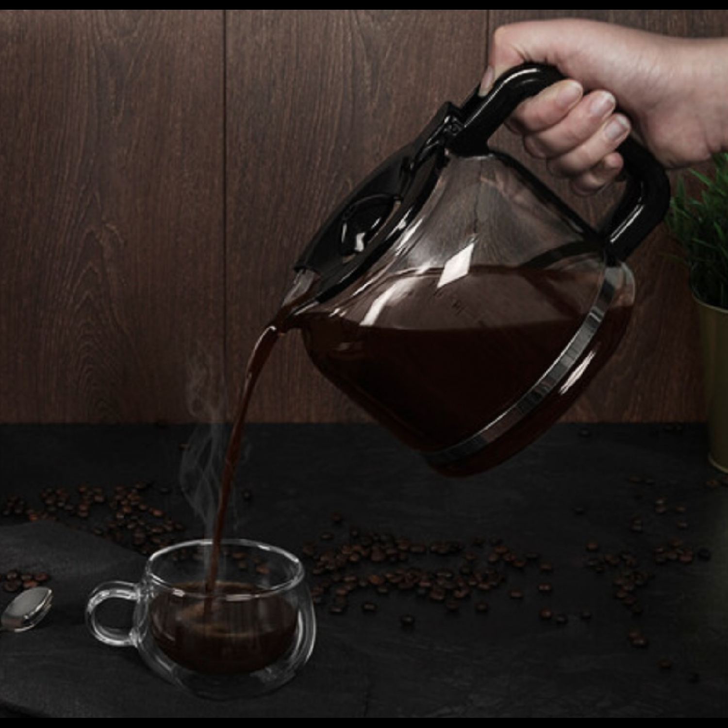 Kawa wlewana do szklanki z karafki. Ziarna kawy i łyżka na ciemnej powierzchni.