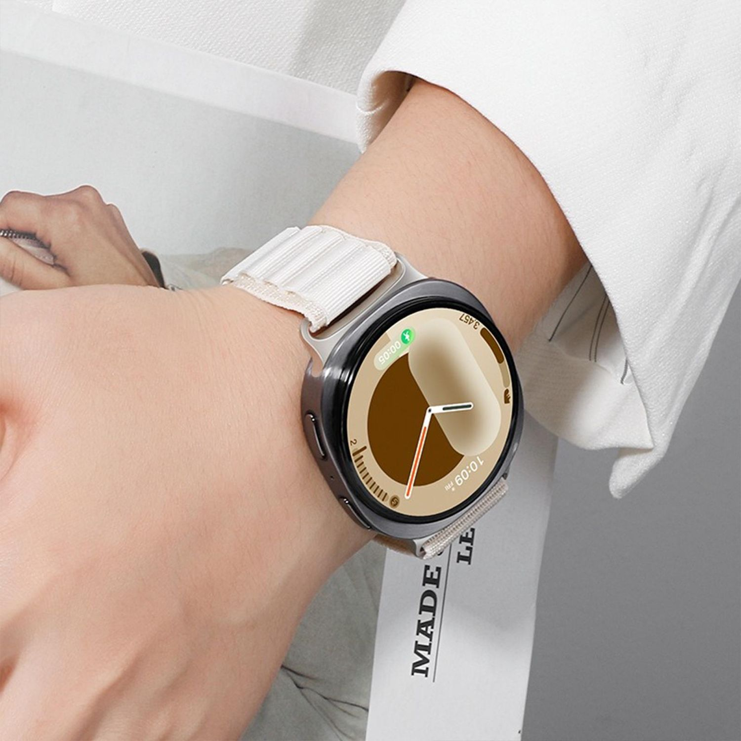 Das Handgelenk einer Person mit einer Smartwatch. Die Uhr hat eine schwarze Lünette und ein helles Armband. Die angezeigte Uhrzeit ist 10:09.