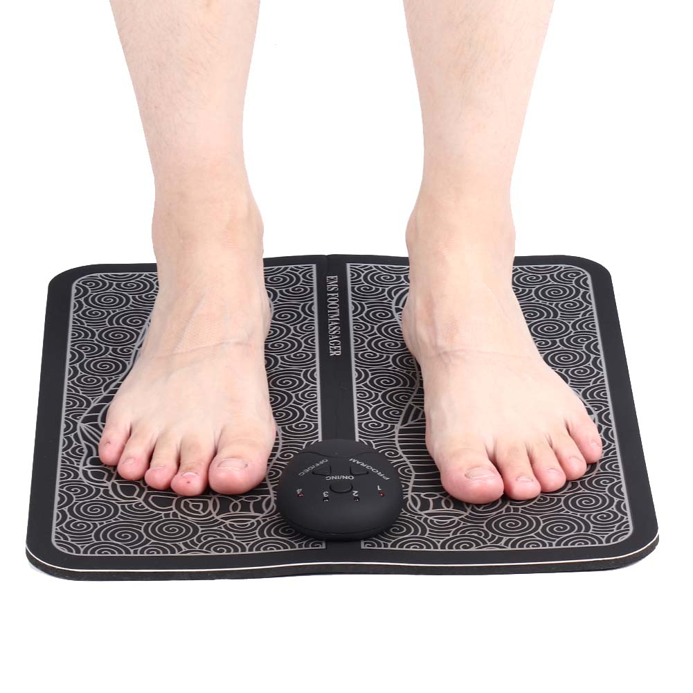 Barfuß auf Fußmassagegerät. Schwarze Matte mit Mustern, Bedienfeld in der Mitte. Text: EMS FOOT MASSAGER.