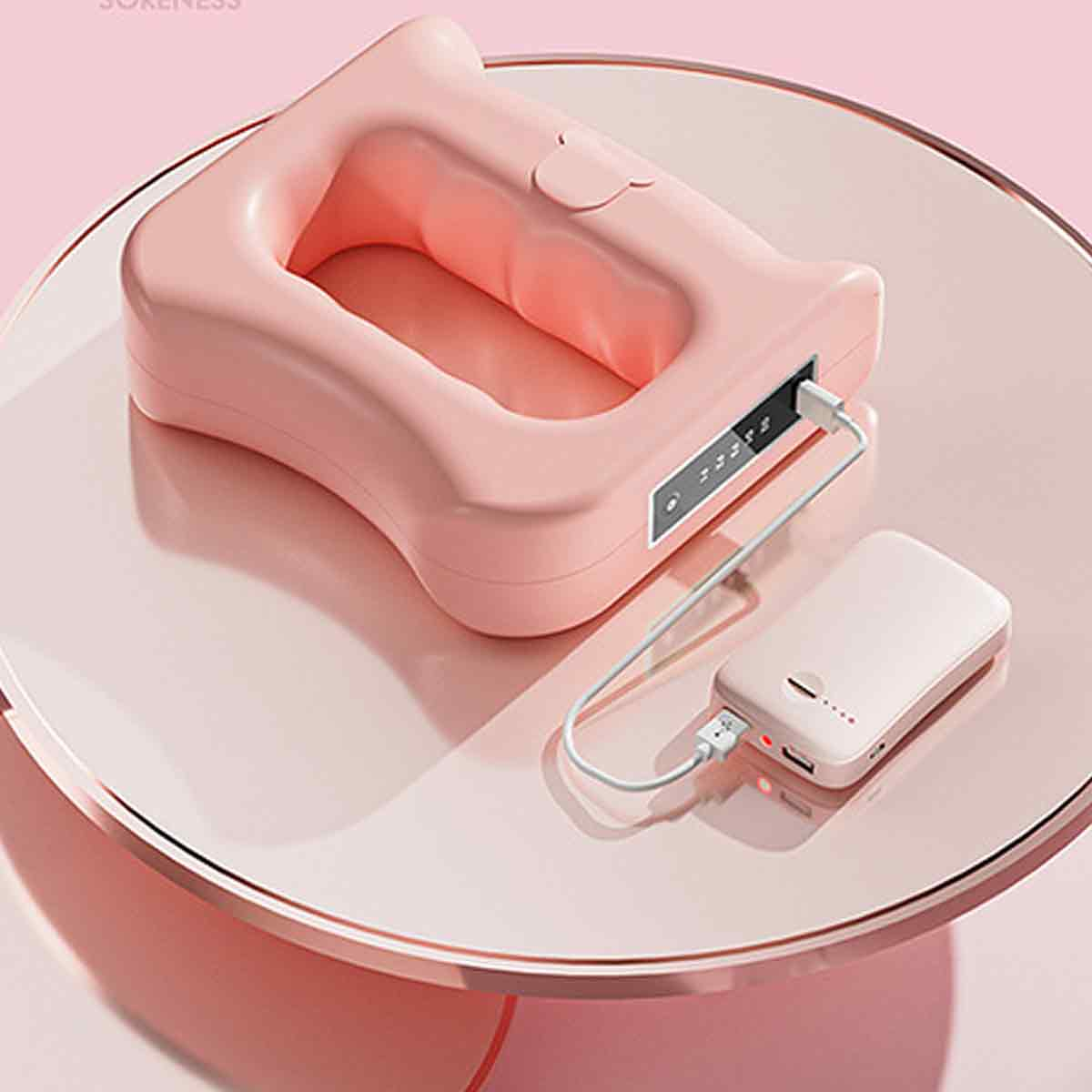 Ein rosafarbenes Massagegerät und eine Powerbank befinden sich auf einer rosa Oberfläche. Die Powerbank ist mit dem Gerät verbunden.